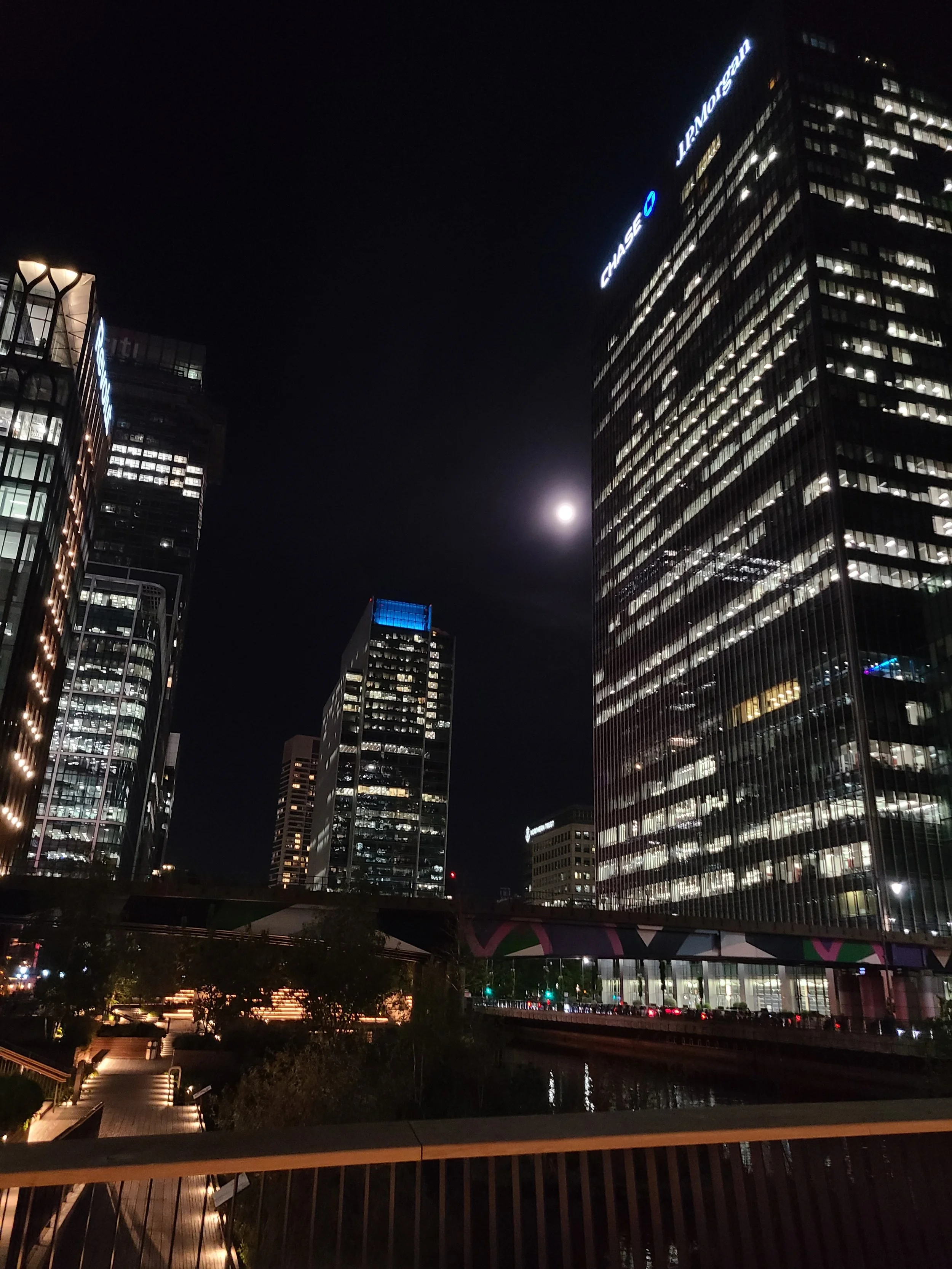 Nighttime cityscape with tall, illuminated skyscrapers, including Chase and Lendlease buildings, and a bright moon in the sky.