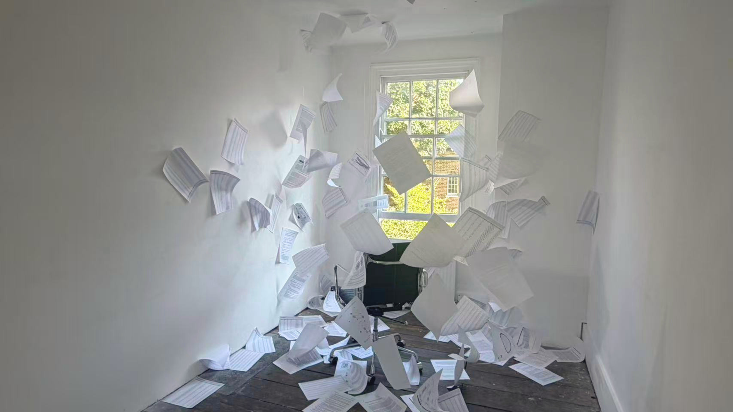 Office room with white walls and window, papers flying and scattered across the floor and mid-air.