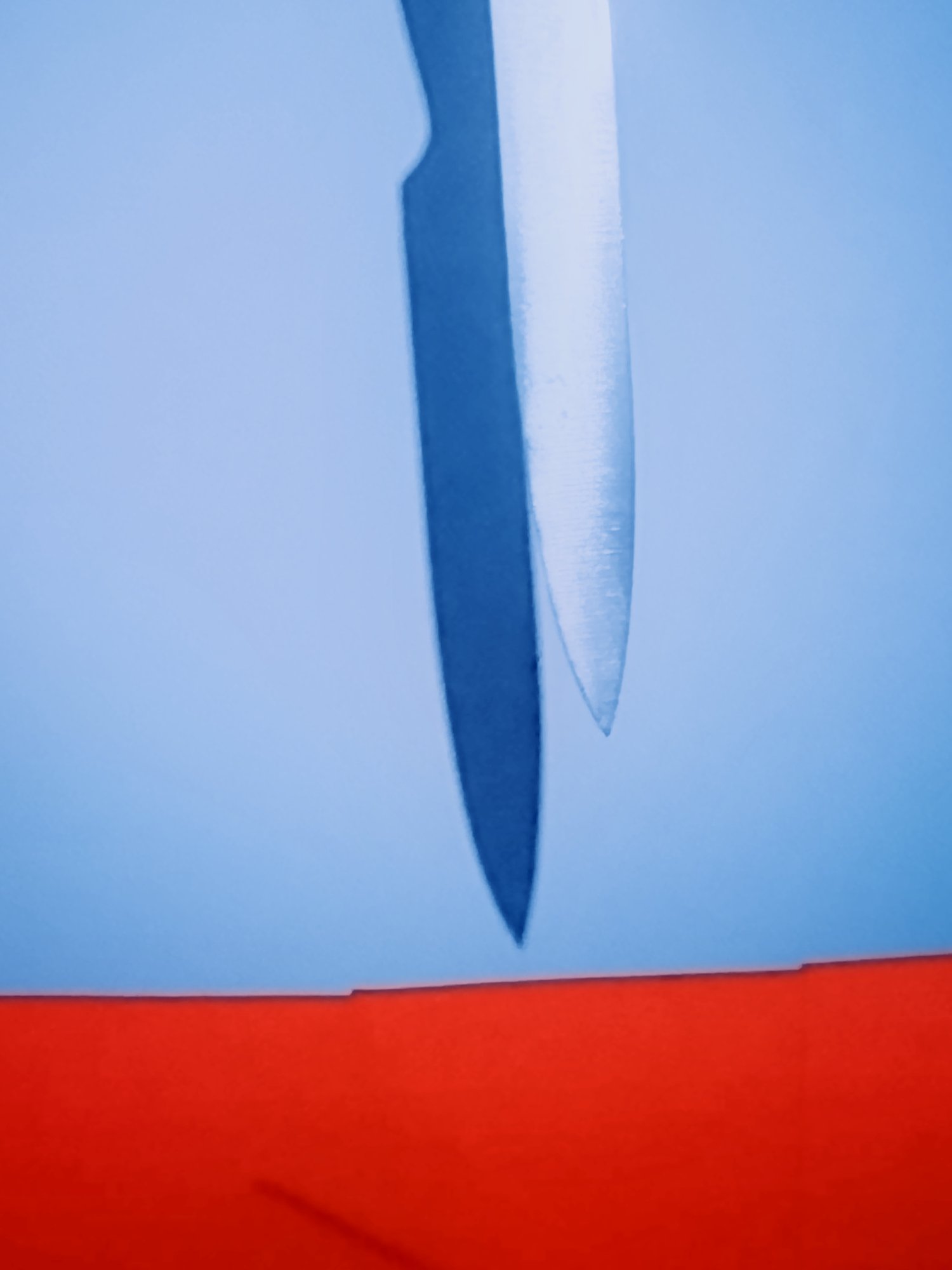 Close-up of a blue and silver metallic elongated object, with a red background at the bottom and a blue background at the top, possibly a sharp or pointed item.