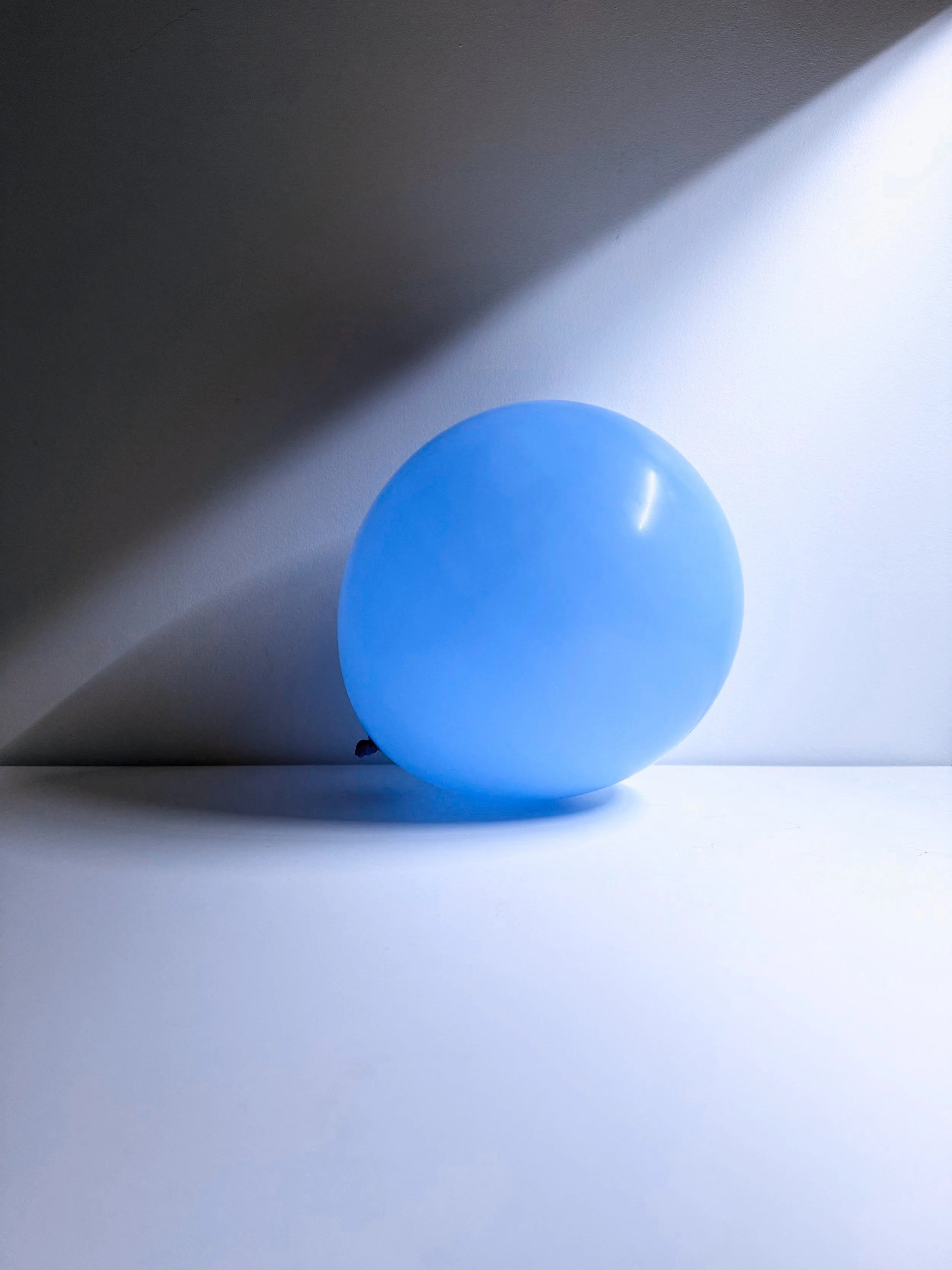 A single blue balloon on a white surface with shadows and light creating a diagonal division in the background.