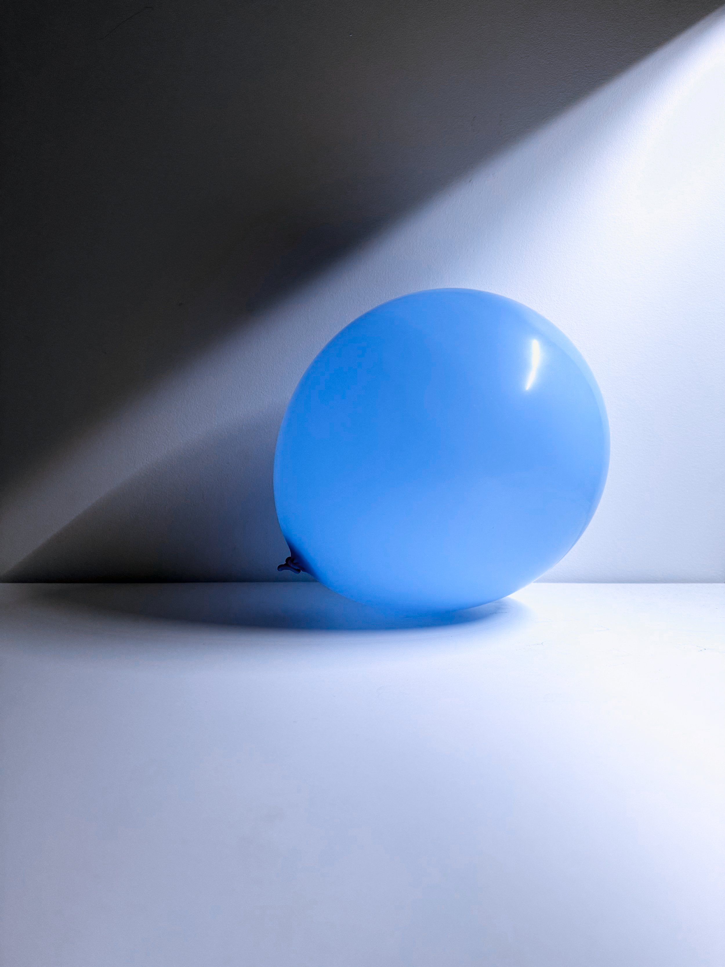 Blue balloon on a white surface with a shadow cast by a diagonal light source.