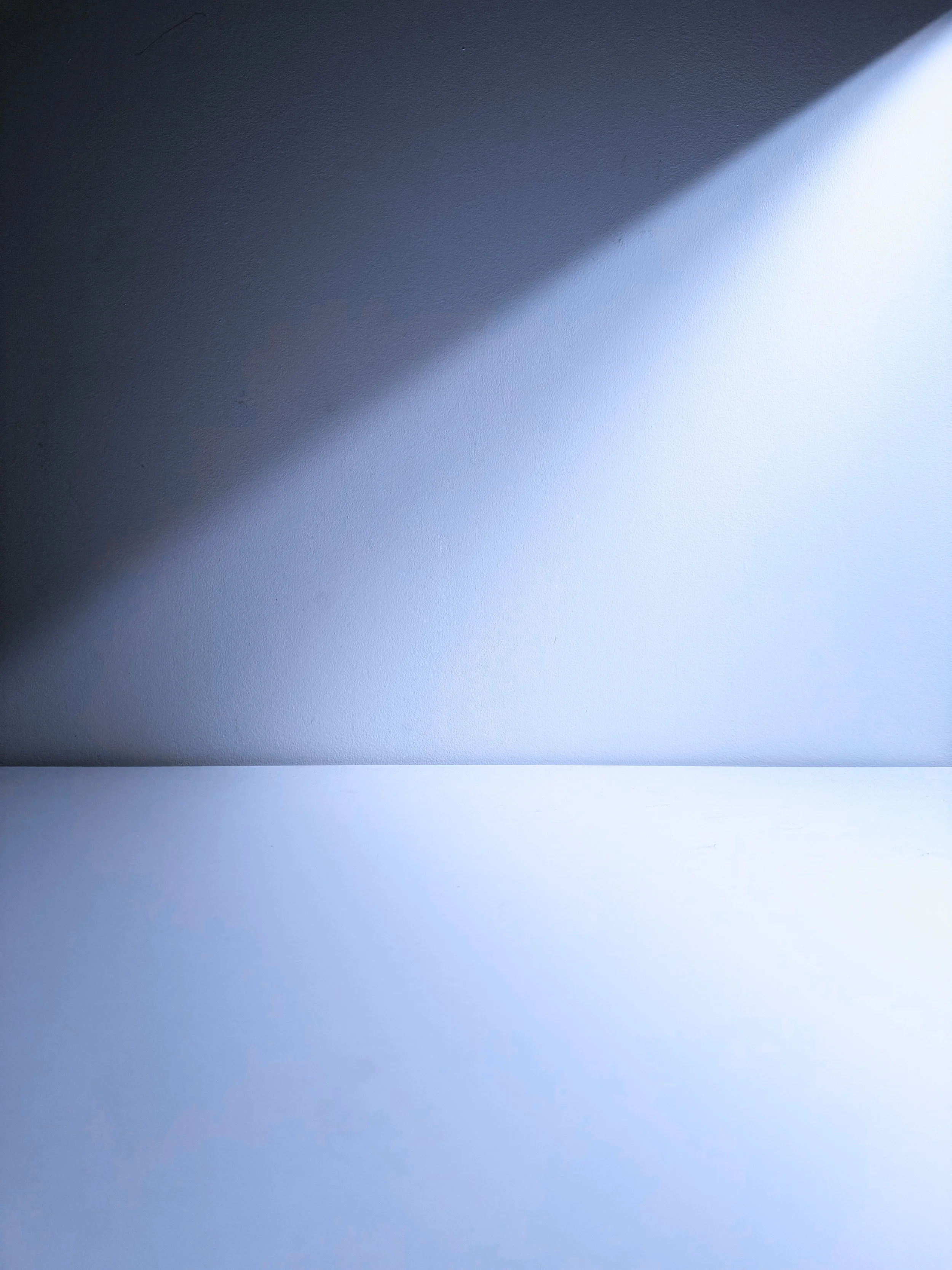 Close-up of a blue wall with diagonal shadows, showing textured surface and gradient light.