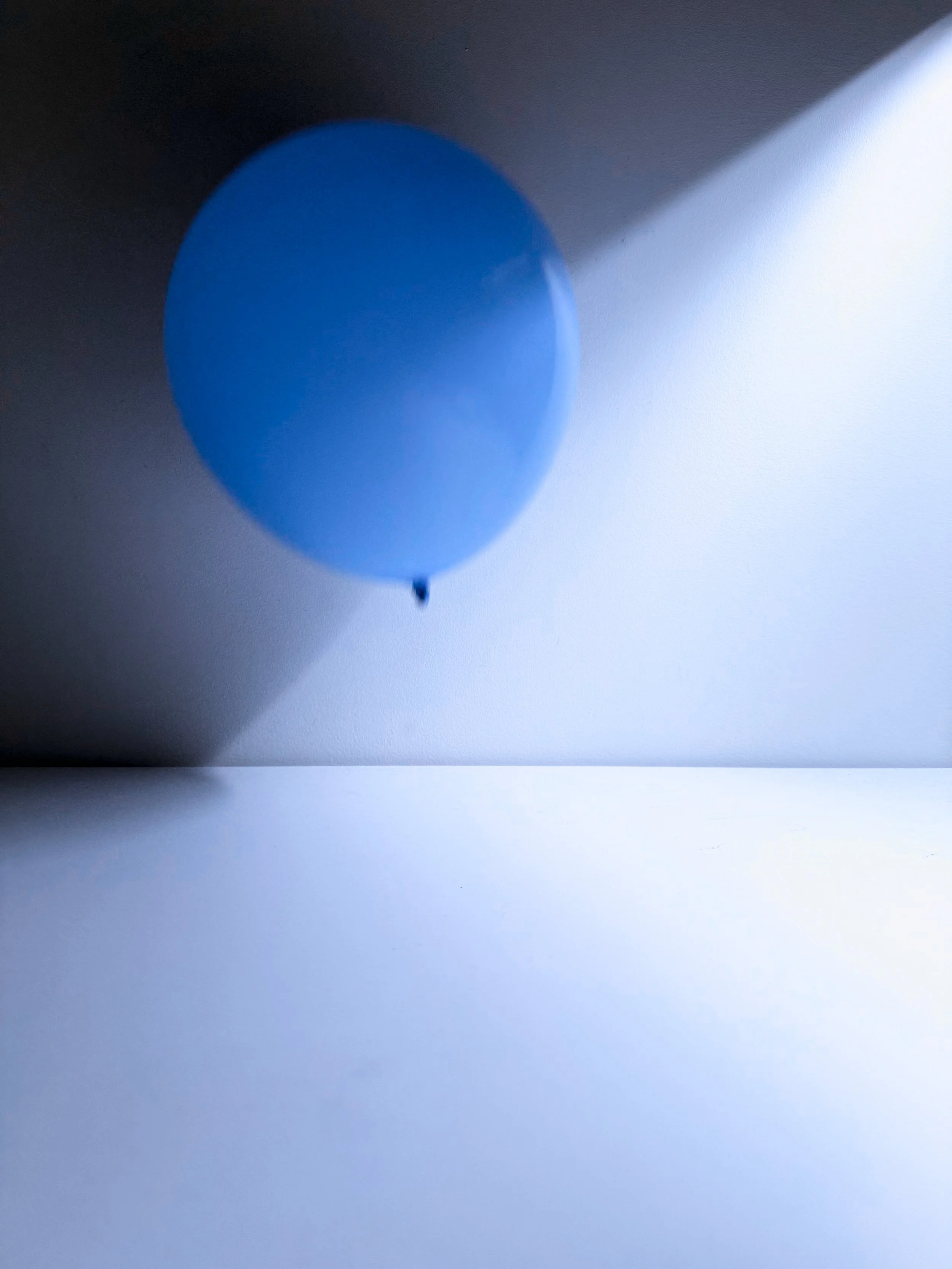 Blue balloon casting a shadow on white and dark gray surface.