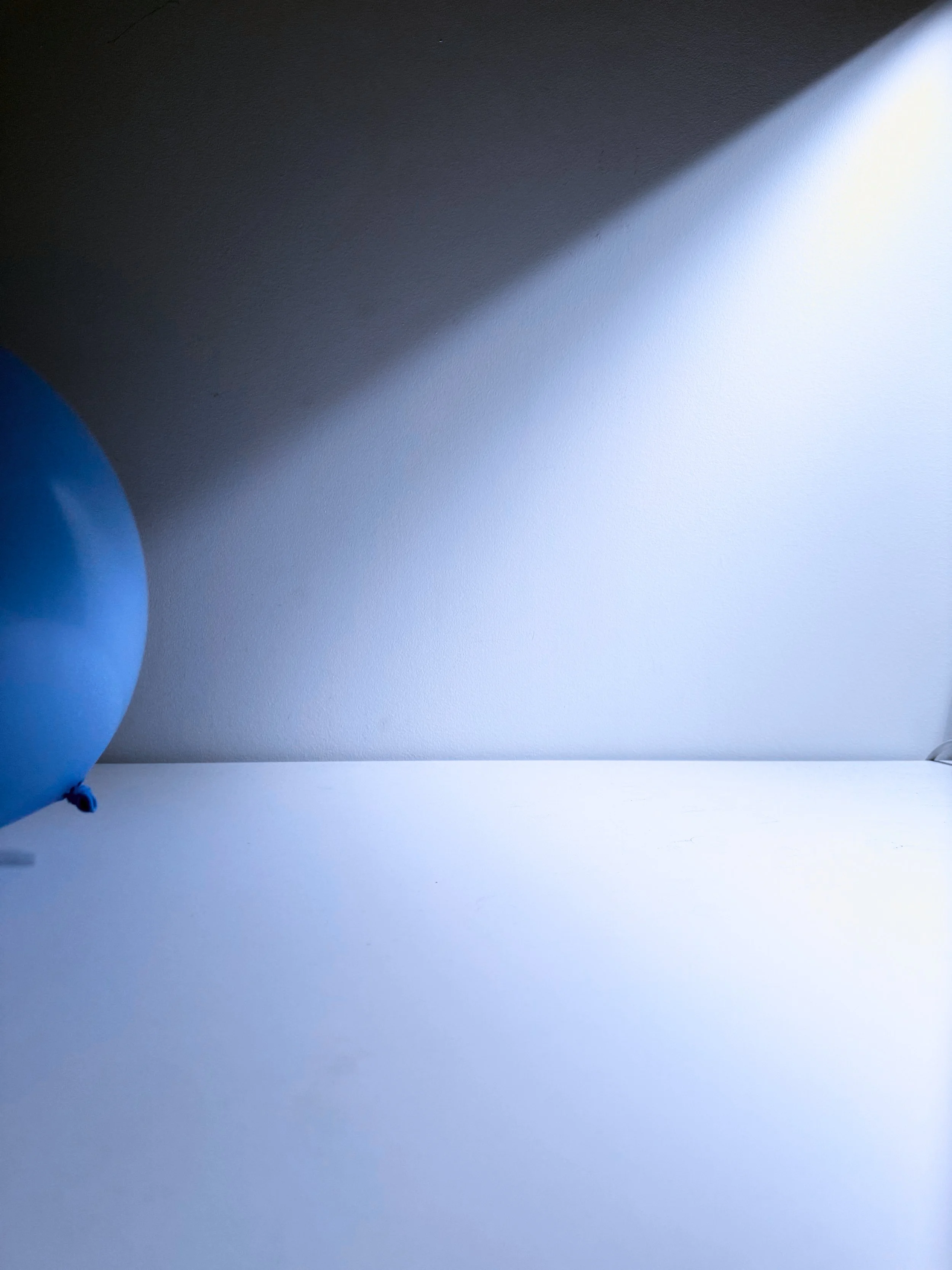 A blue balloon partially visible on the left side of the image against a background with shadowed and lit areas on the wall.
