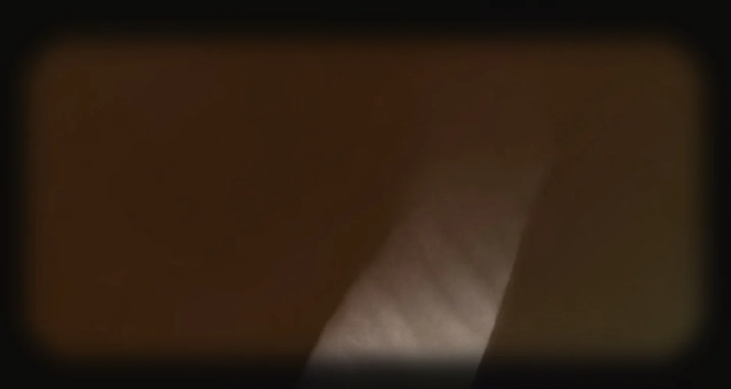 A blurry, dark close-up image with a faint light streak and some indistinct shapes.
