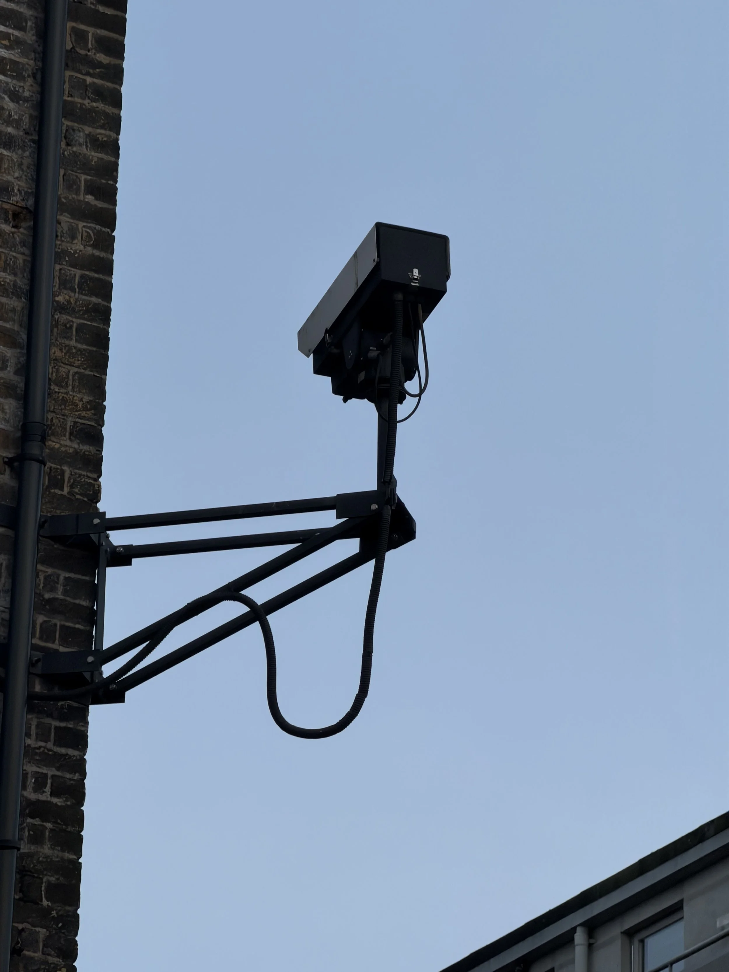 A tall outdoor antenna mounted on the side of a building, with wires hanging from it, against a clear blue sky.