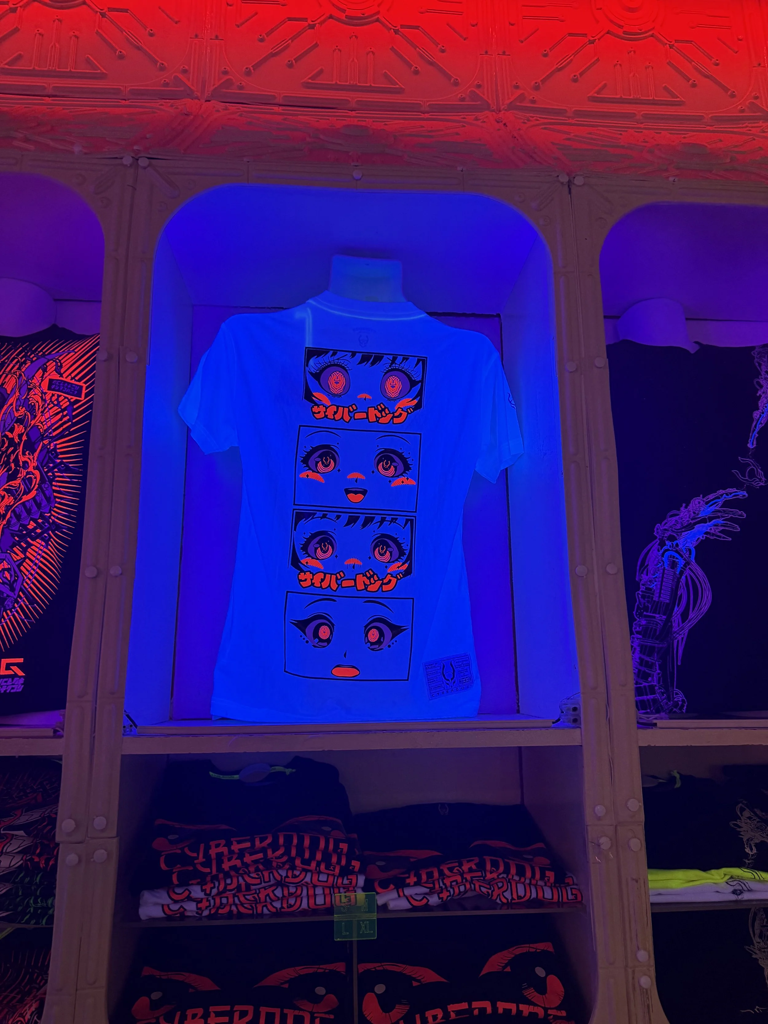 Display of white T-shirts with colorful graphic designs featuring stylized eyes and Japanese characters, surrounded by vibrant, neon-colored lighting effects.