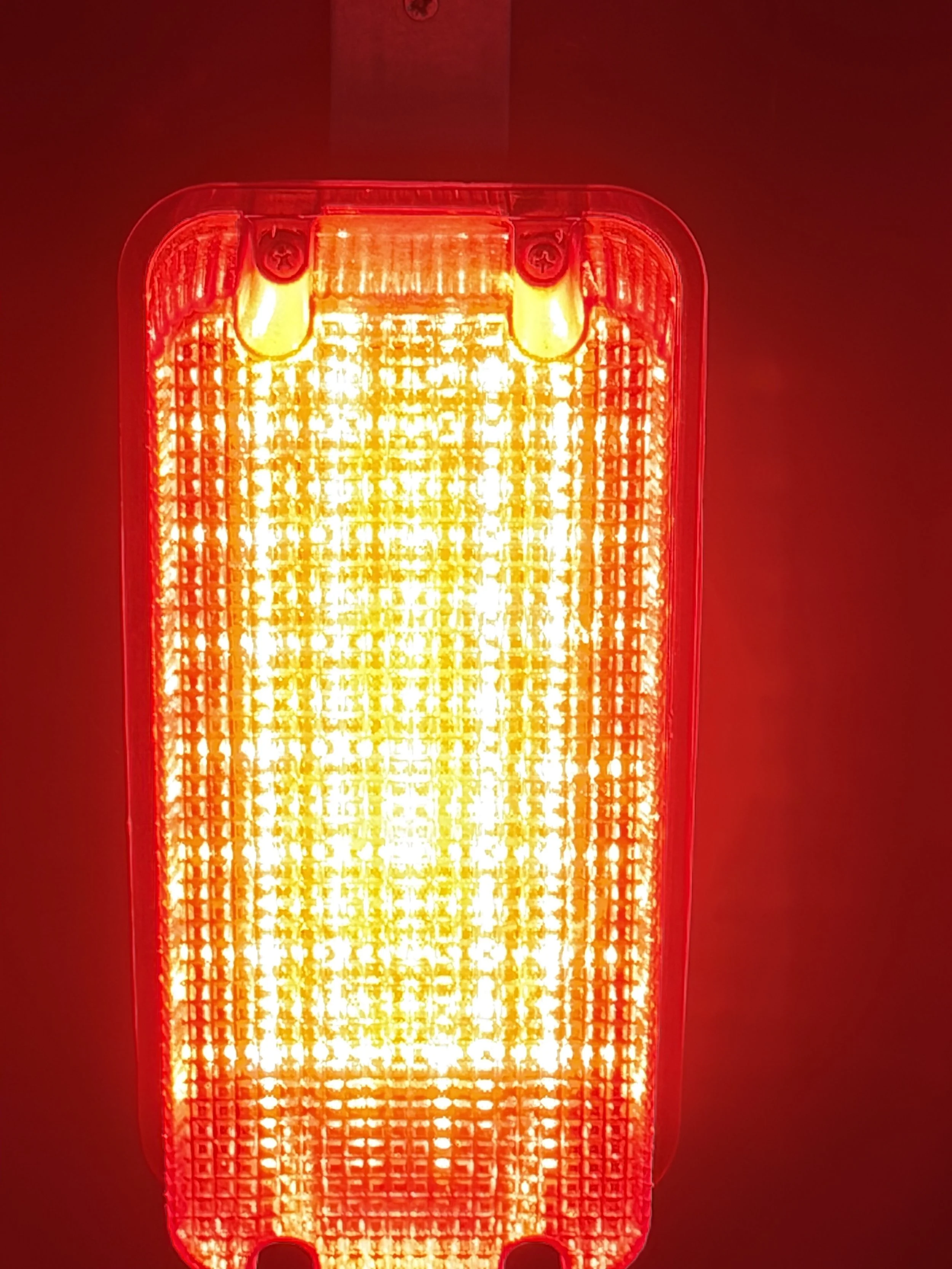 Close-up of a red and yellow illuminated emergency or warning light, with a grid pattern on its surface, mounted on a wall.