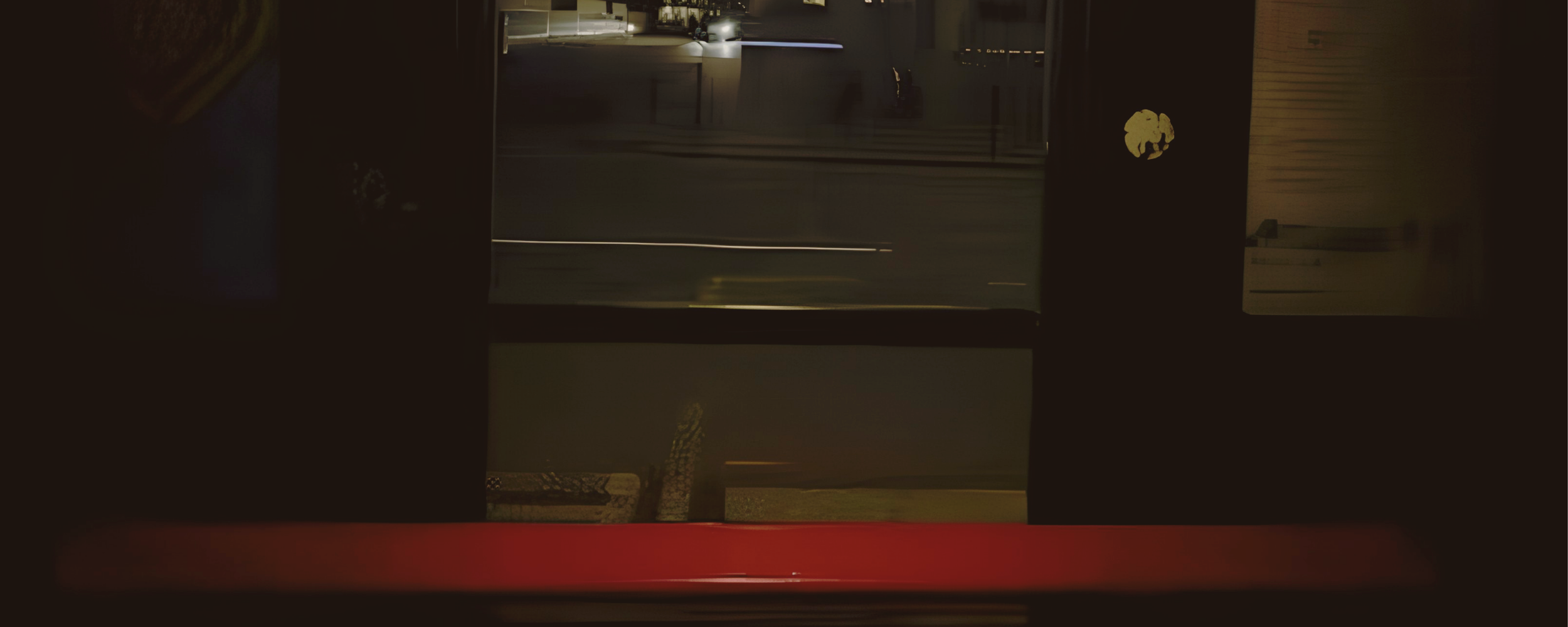 Nighttime view of a street scene through a window, with buildings, streetlights, and a car parked on the road.