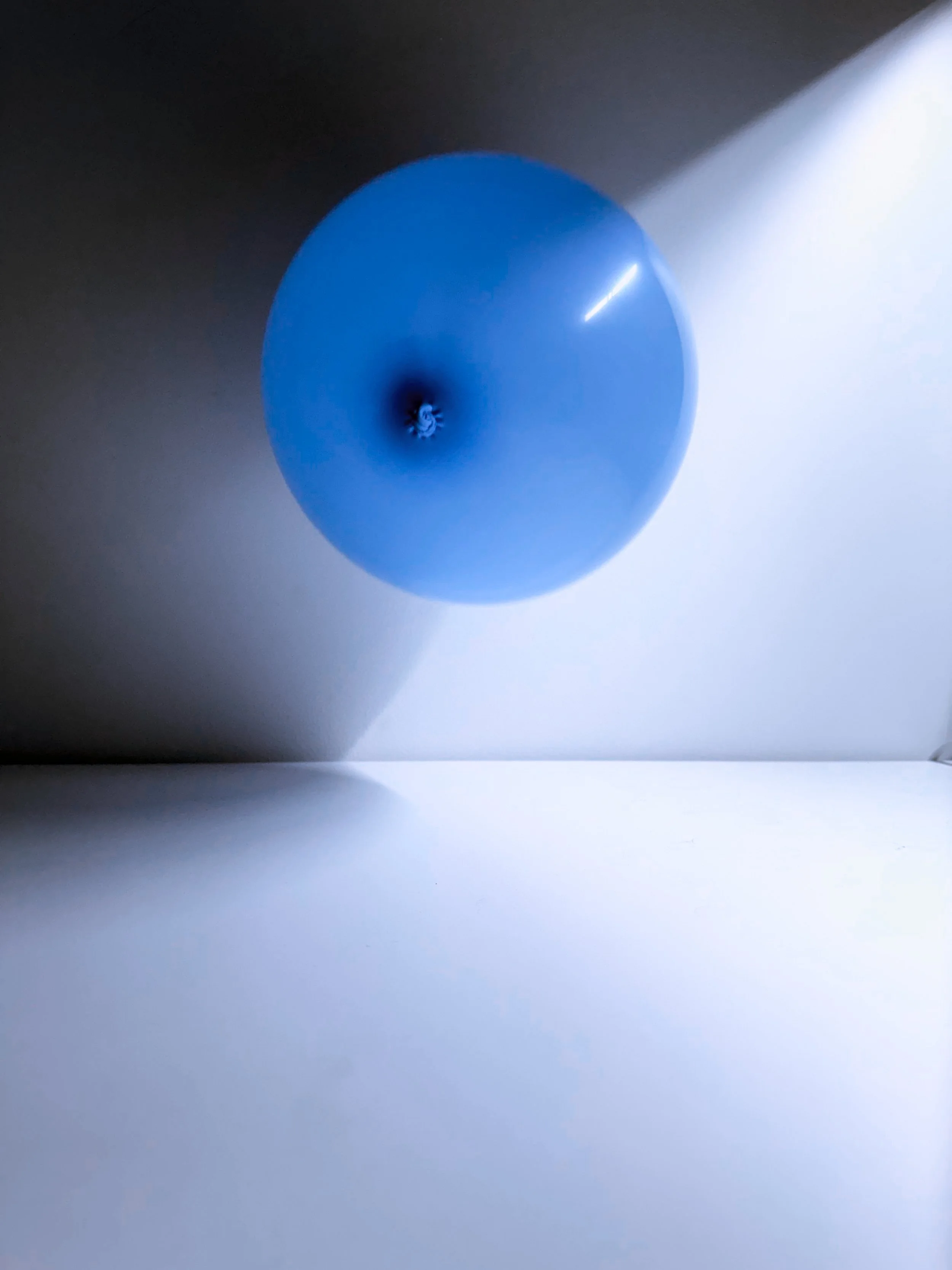Blue balloon floating against a plain background with shadows and light reflections.
