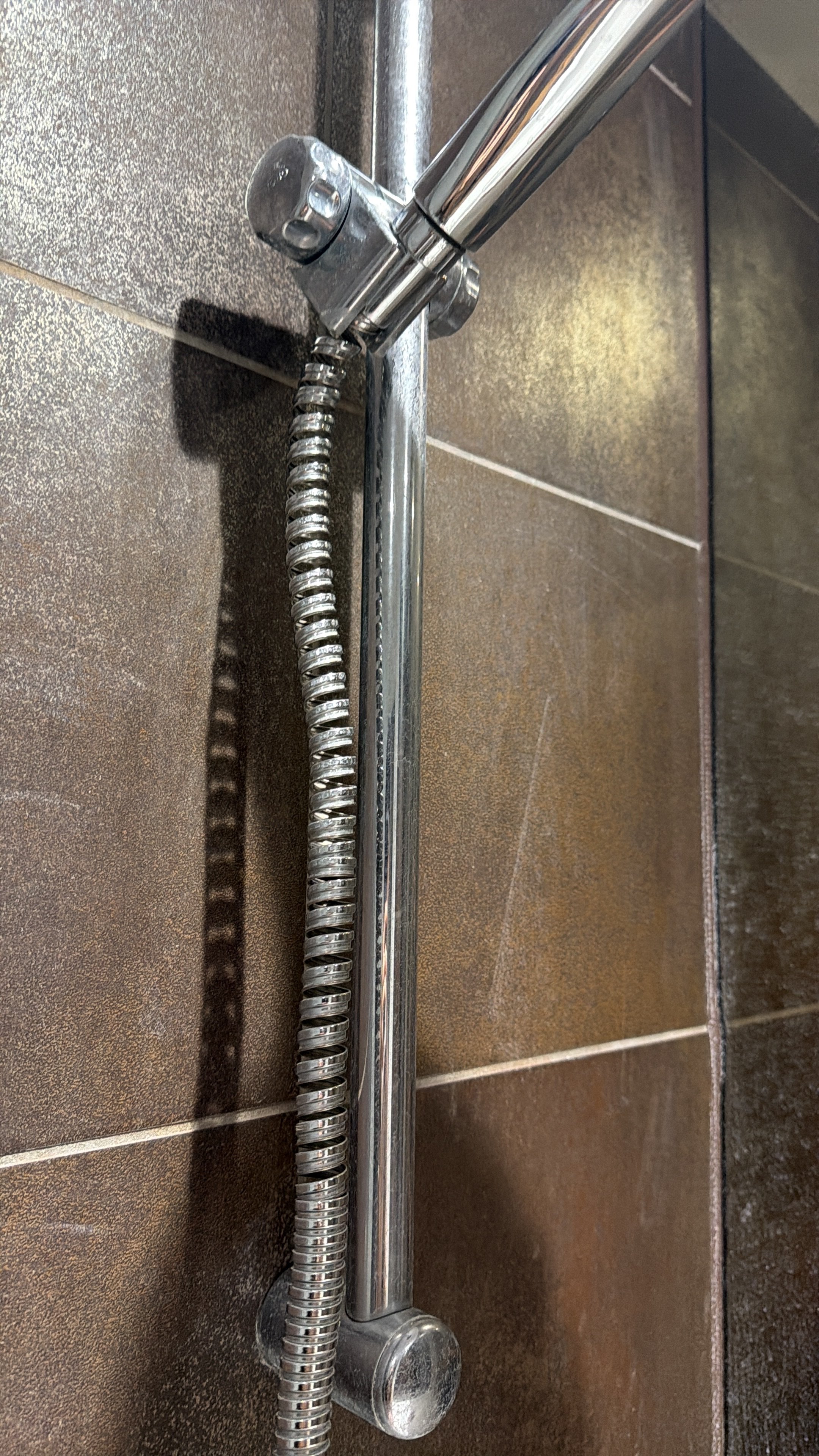 Close-up photo of the shower faucet handle and flexible hose on a brown tiled wall.