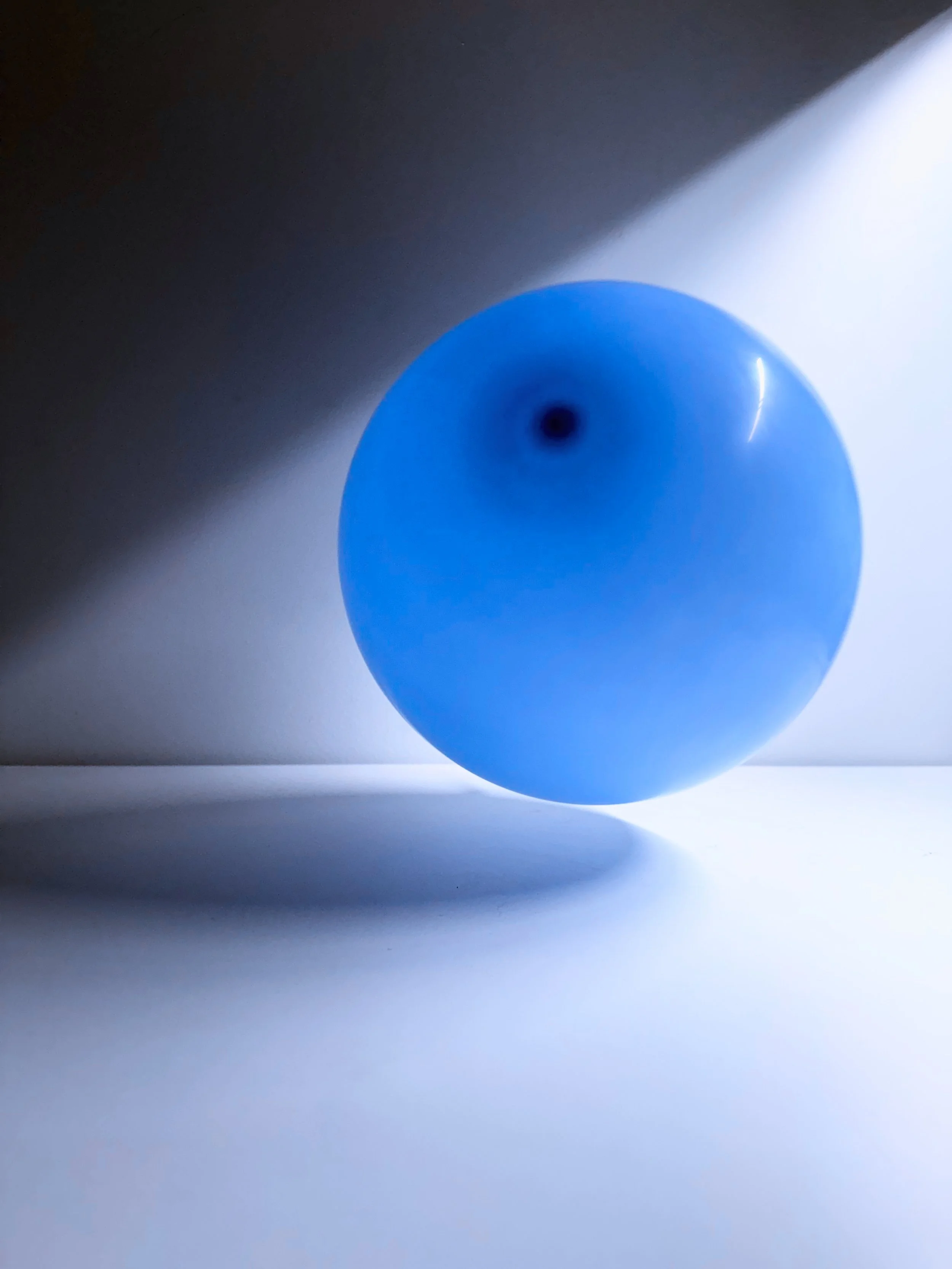 A blue spherical object with a dark circular center, casting a shadow on a light gray surface with a gradient shadow extending from the object.