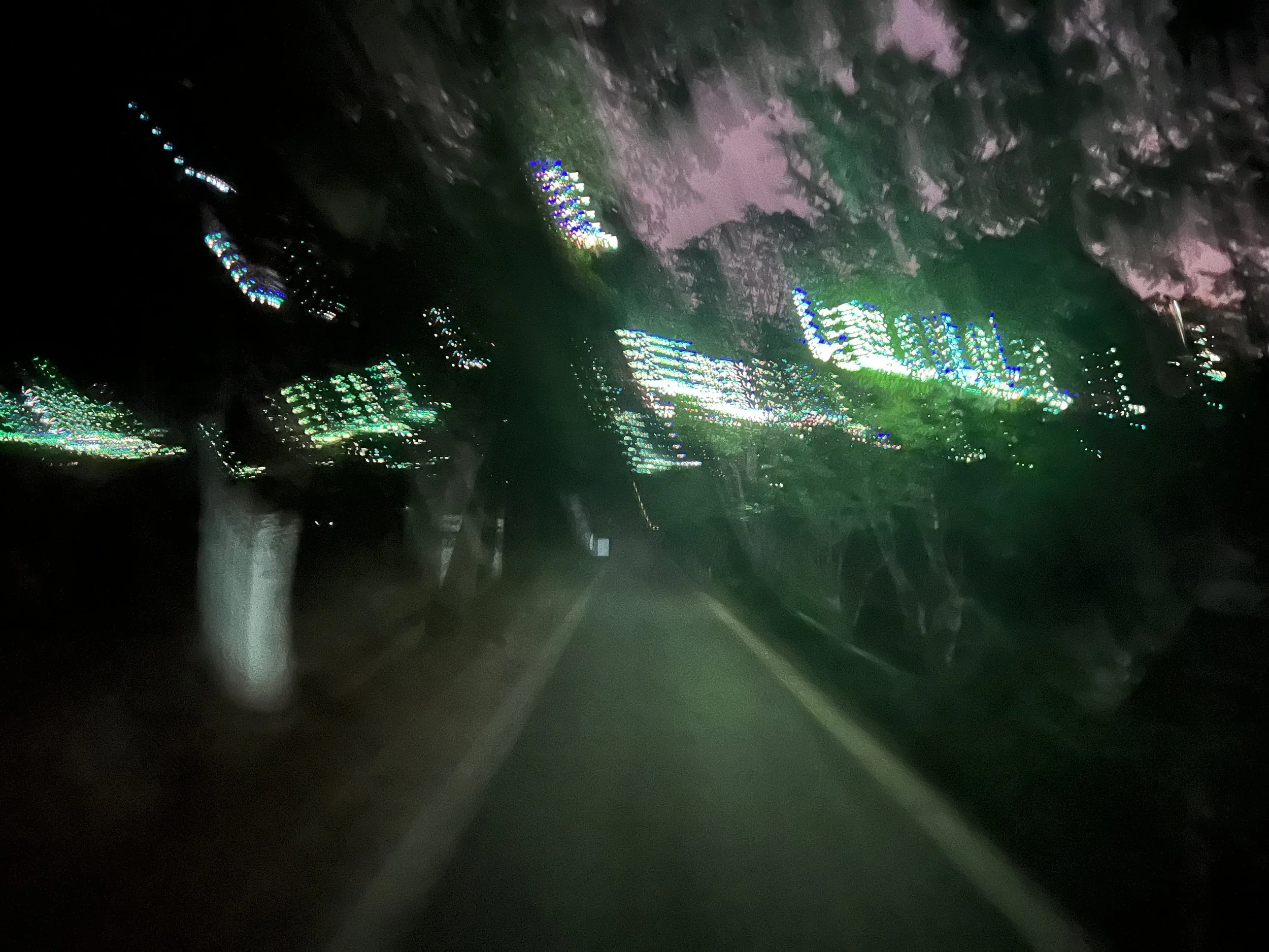 A car windshield with rain droplets, reflecting colorful city lights during nighttime.