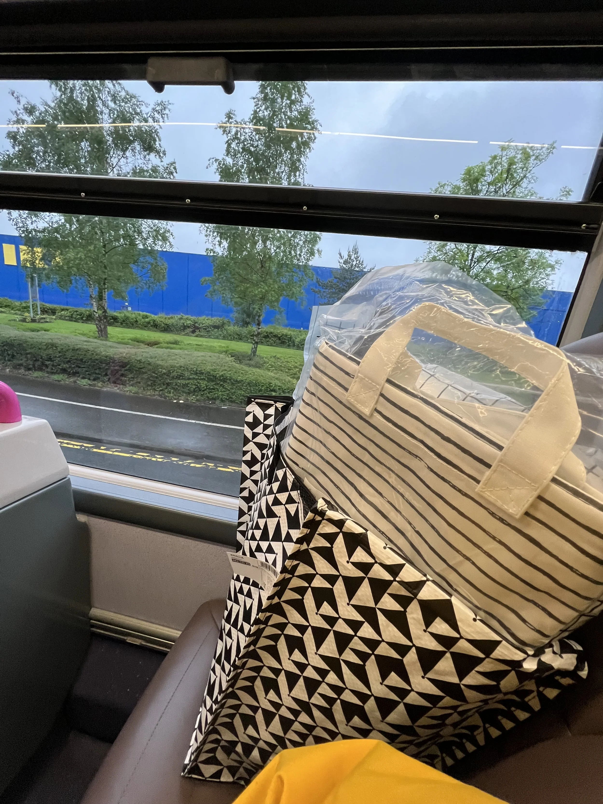 View through a bus window showing trees, a blue building, and bags on the seat.