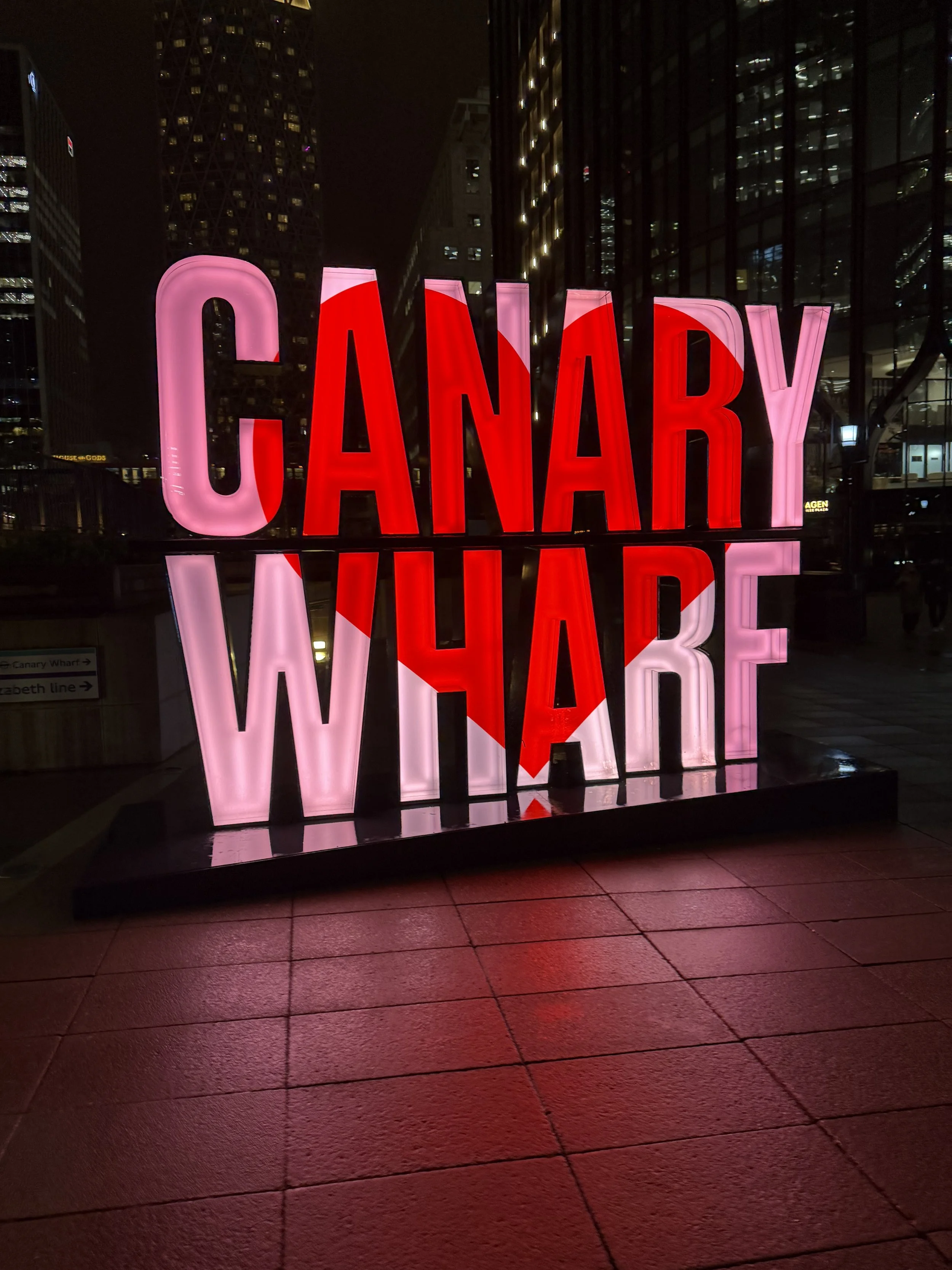 Nighttime cityscape with illuminated 'CANDY' sign in pink and red neon lights reflecting on wet pavement
