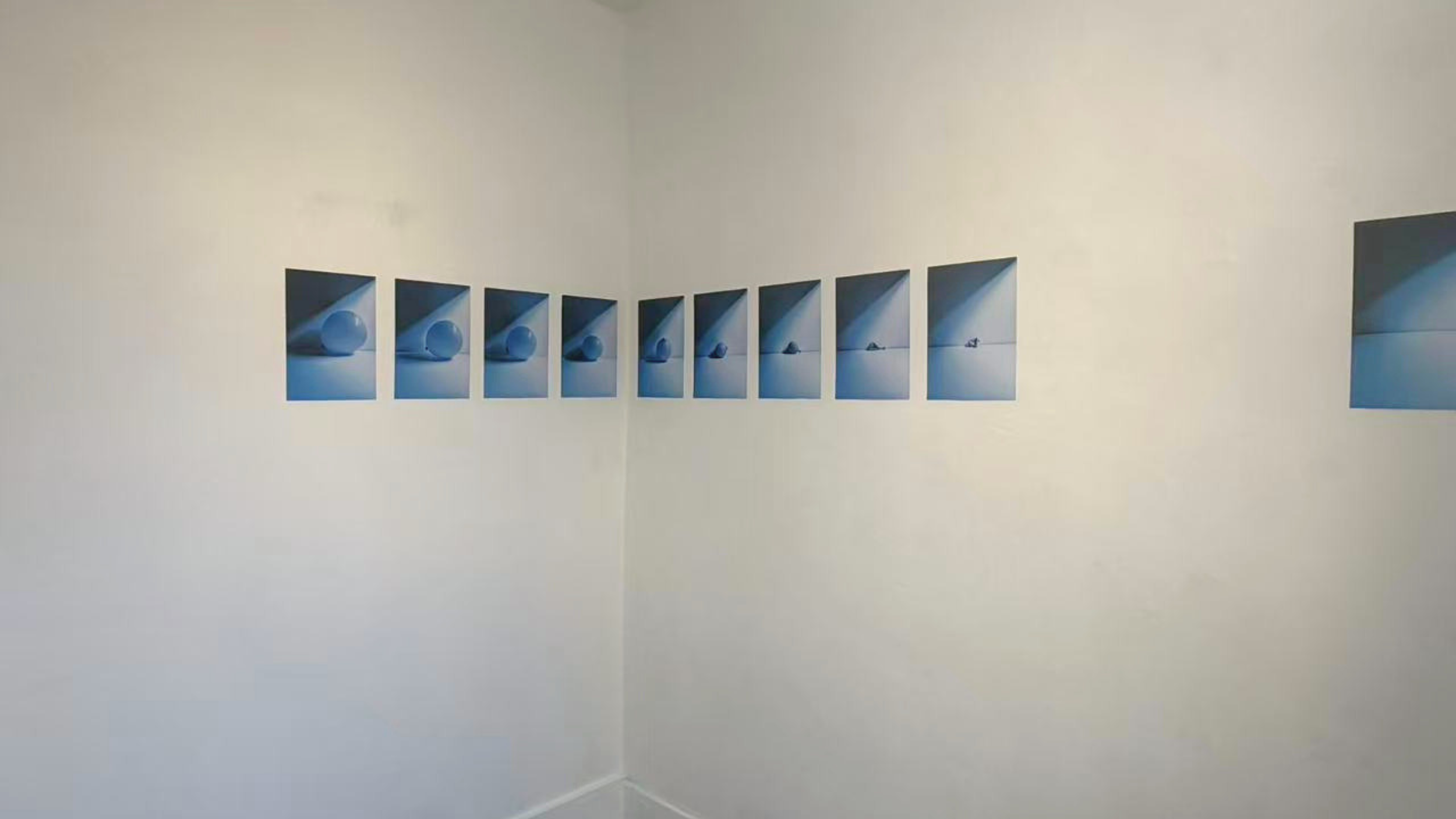 A series of eight blue photographs of a spherical object in a white box on a white wall, arranged in a horizontal line.