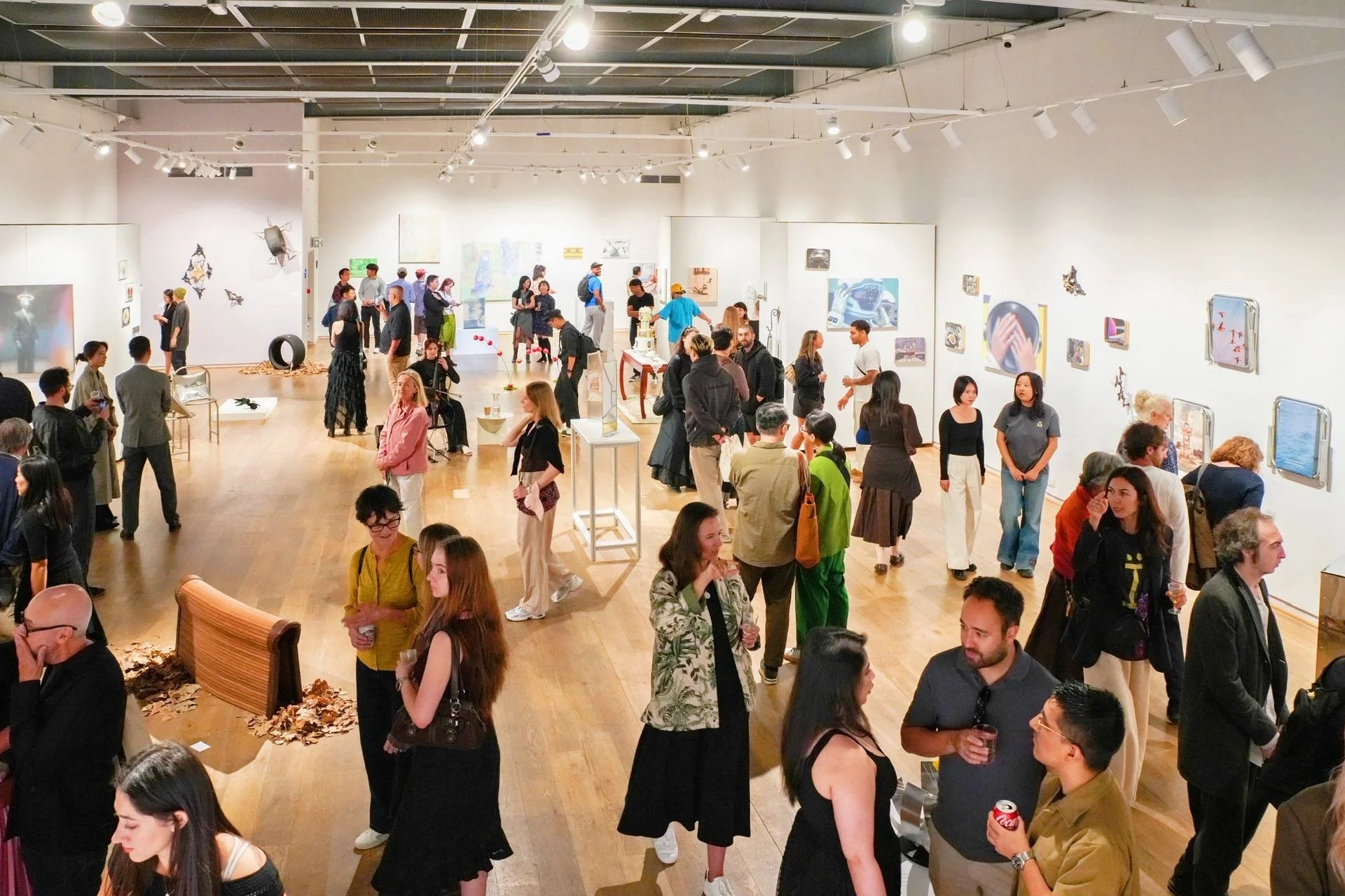 People attending an art gallery exhibition, viewing and discussing artwork displayed on white walls.