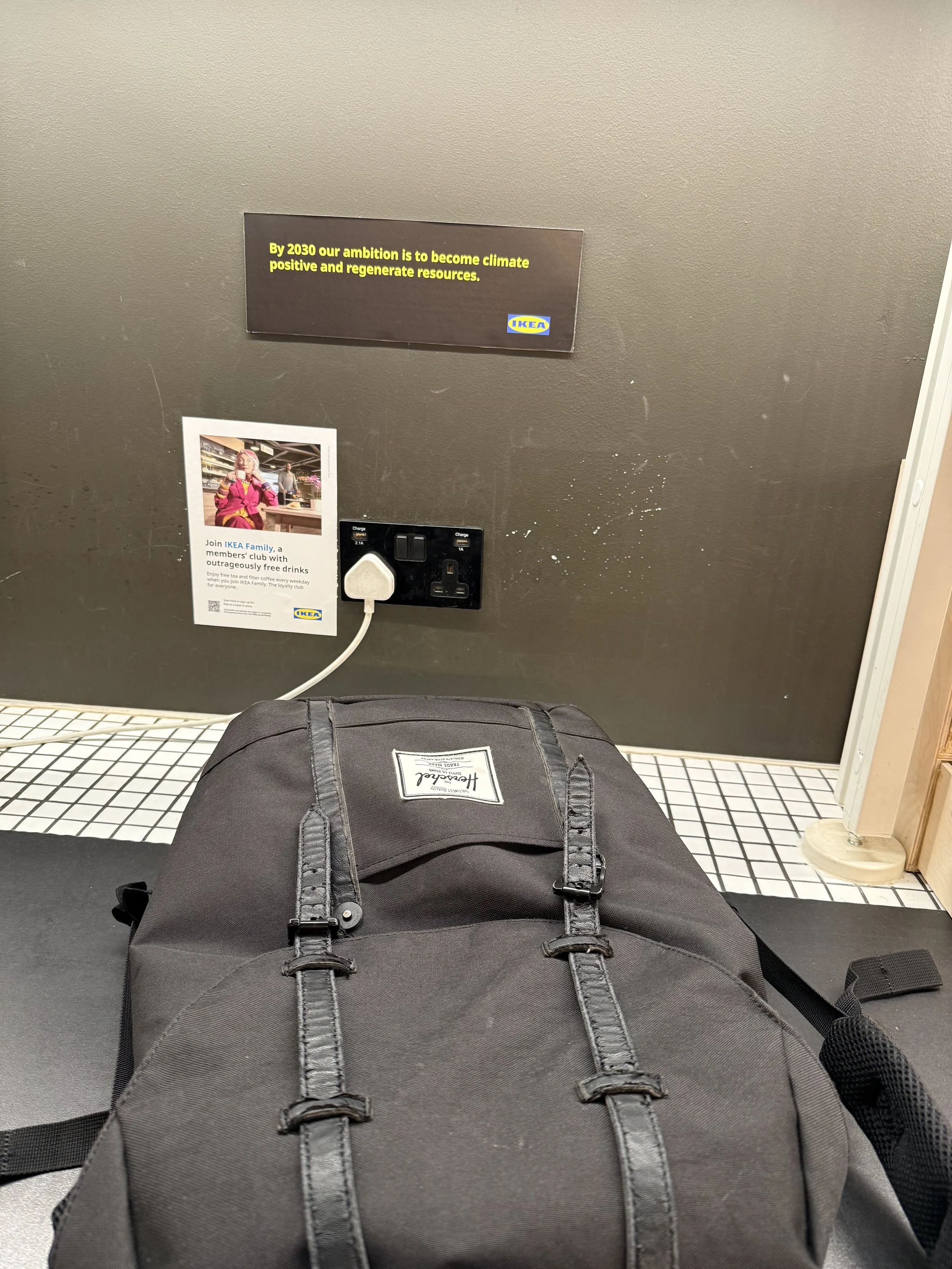 Top of black backpack on floor inside IKEA store, with wall and posters in background.