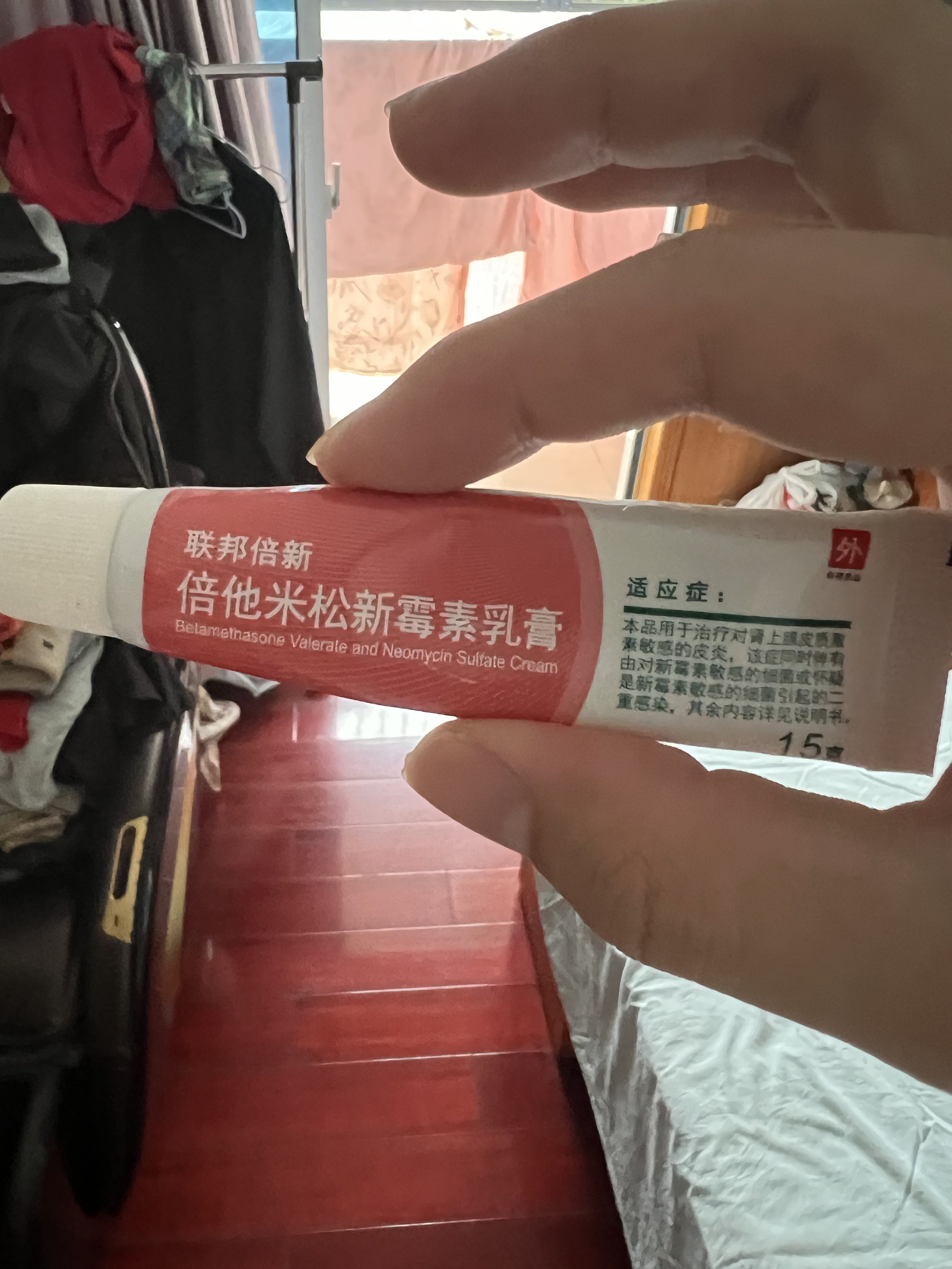 Person holding a tube of Belarusian ointment in a room with clothes and luggage in the background.