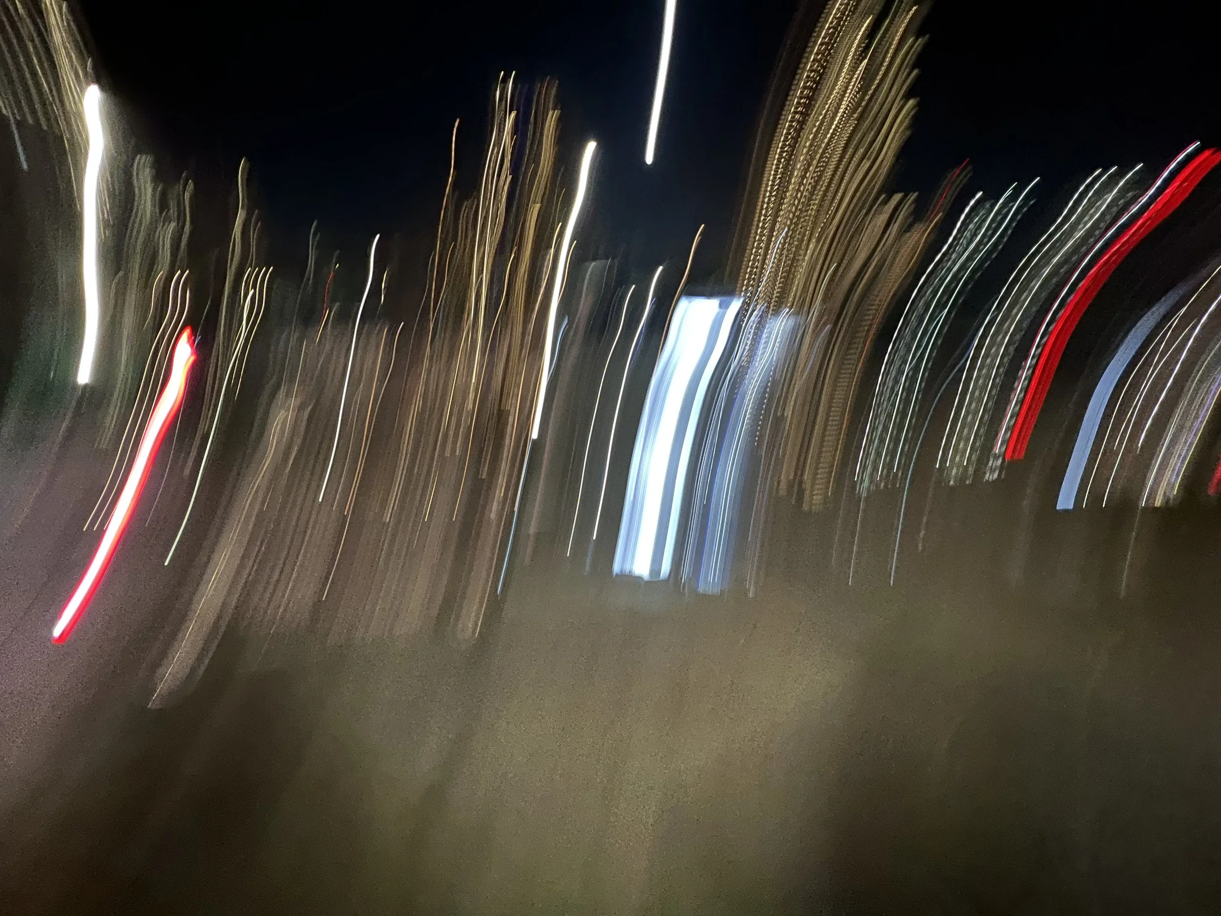 Nighttime city street with blurred moving lights and streaks of red, white, yellow, and blue from vehicle headlights and taillights.