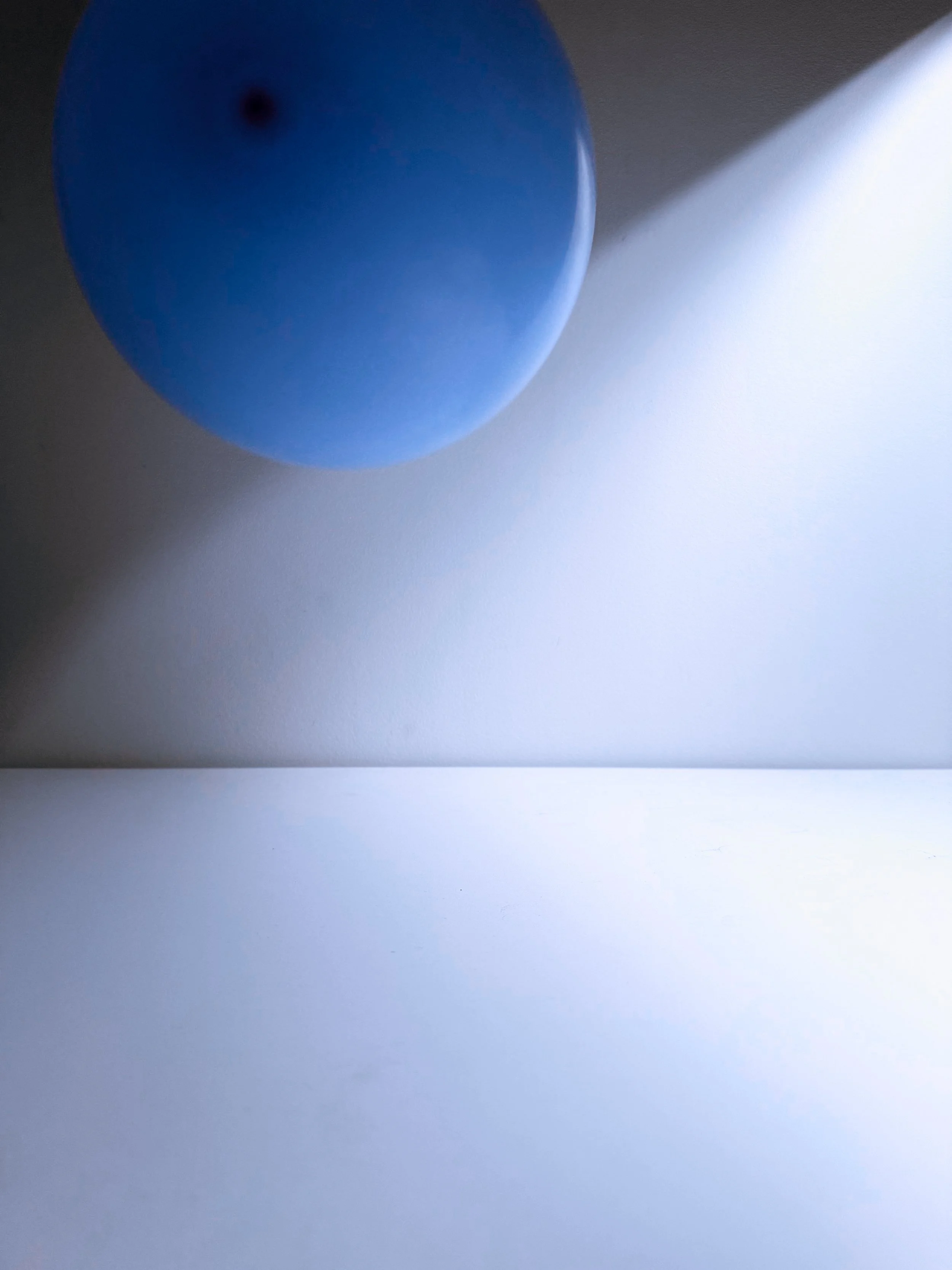 Close-up of a blue balloon casting a shadow on a white surface with a gray background.