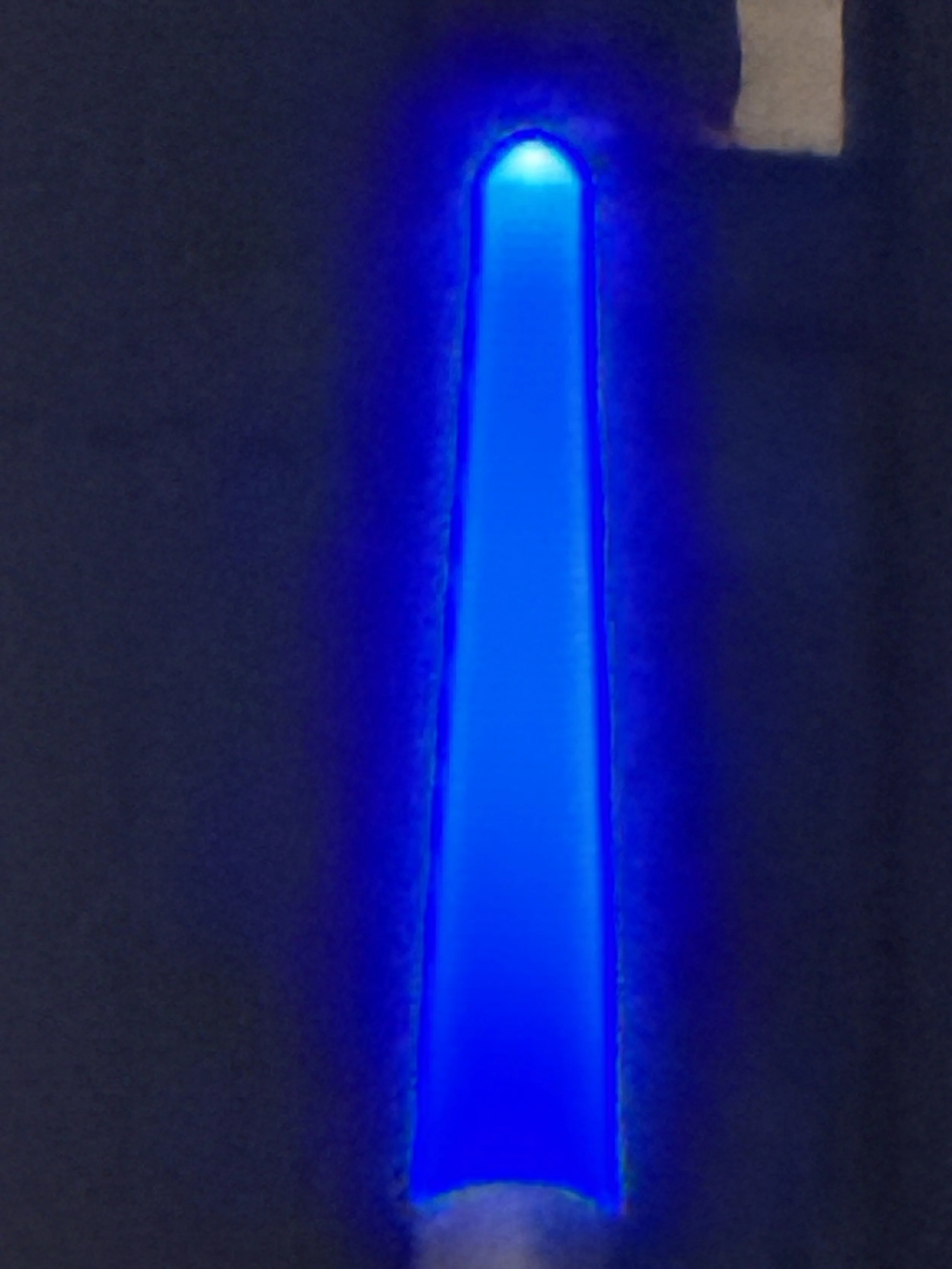 A blue LED light strip mounted on a dark wall, casting a bright blue glow and reflection on the surface below.