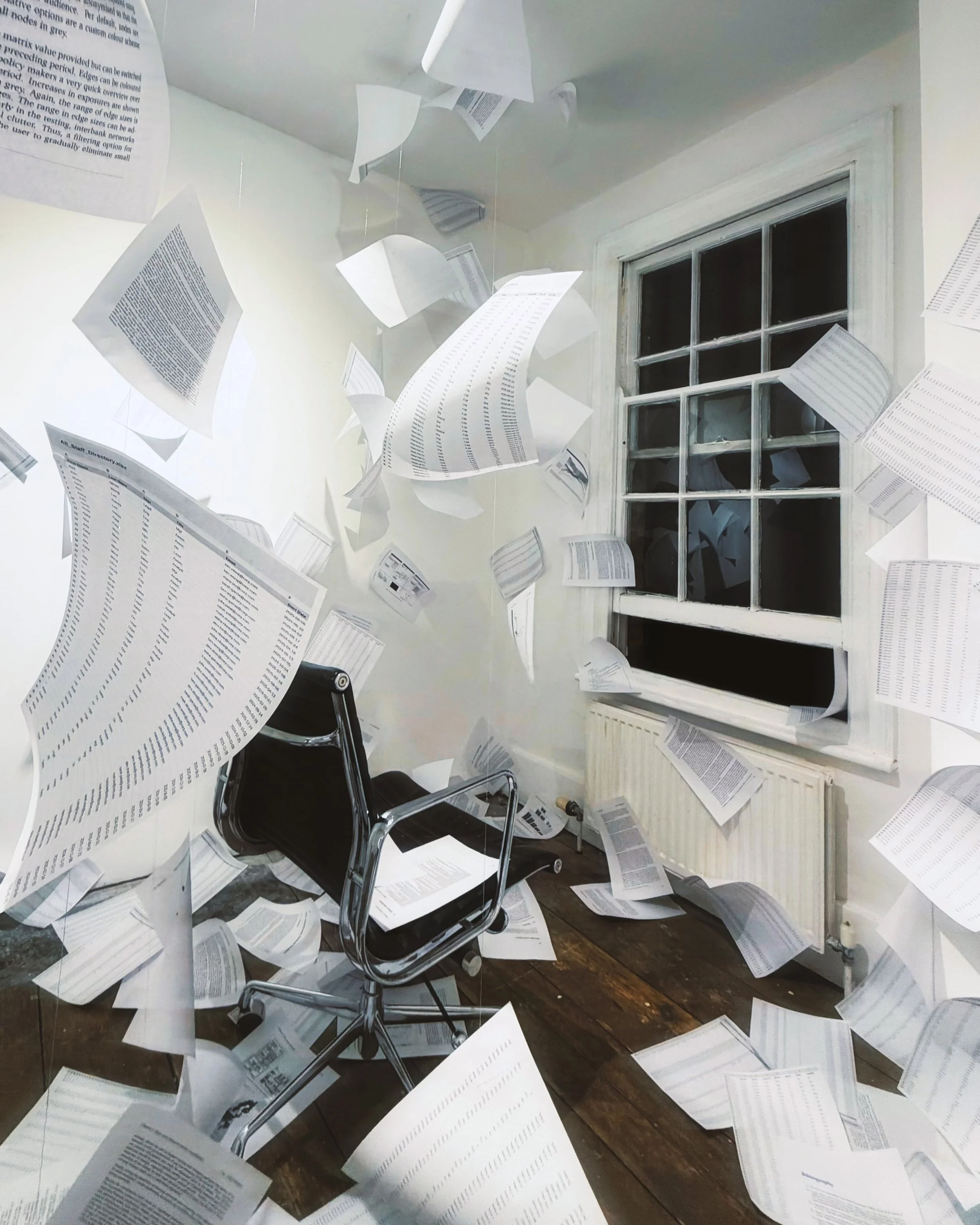 Page documents and papers flying around a room, with a black office chair and a window in the background.