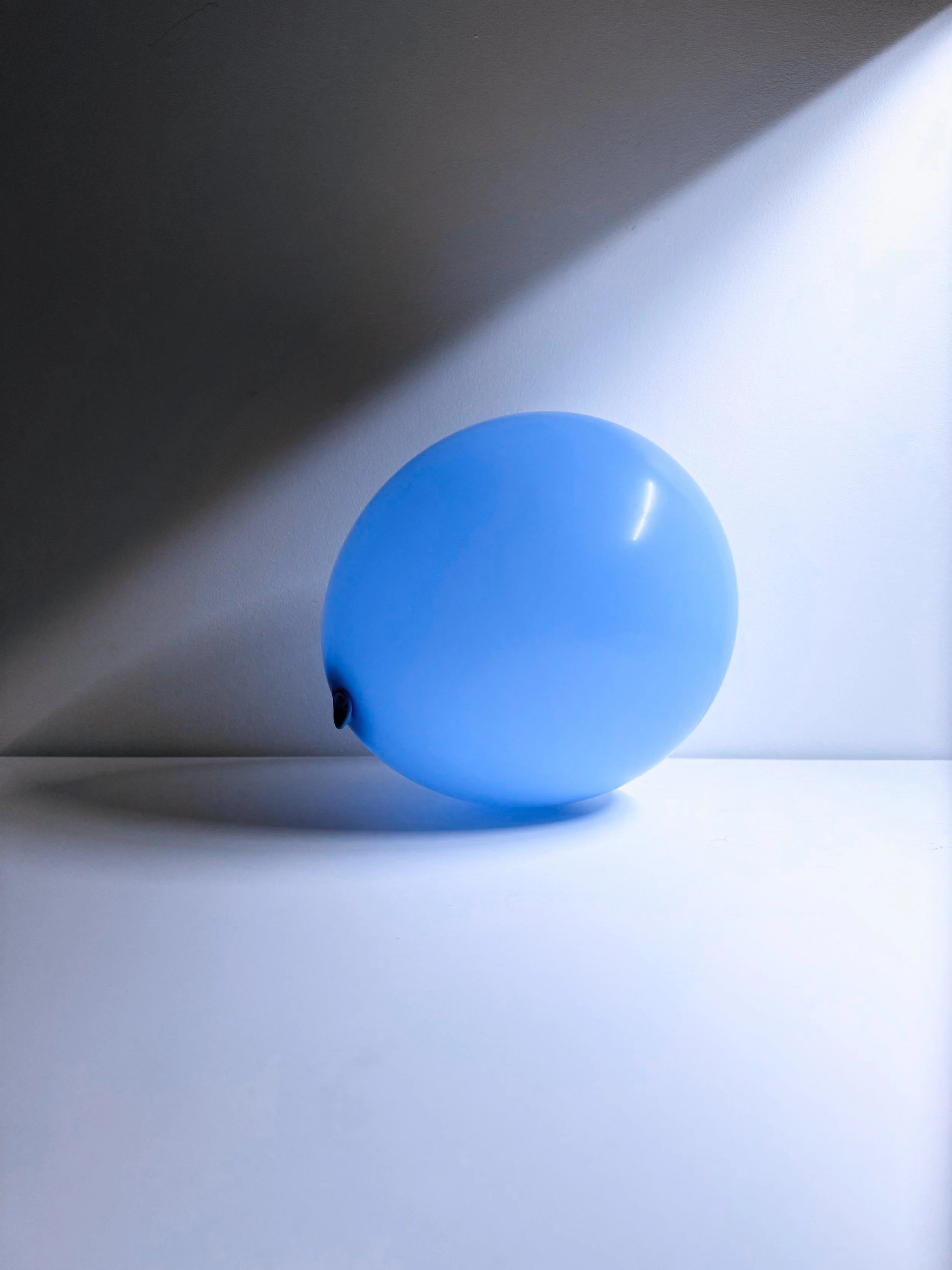 A blue balloon on a white surface with a gradient shadow on the background.