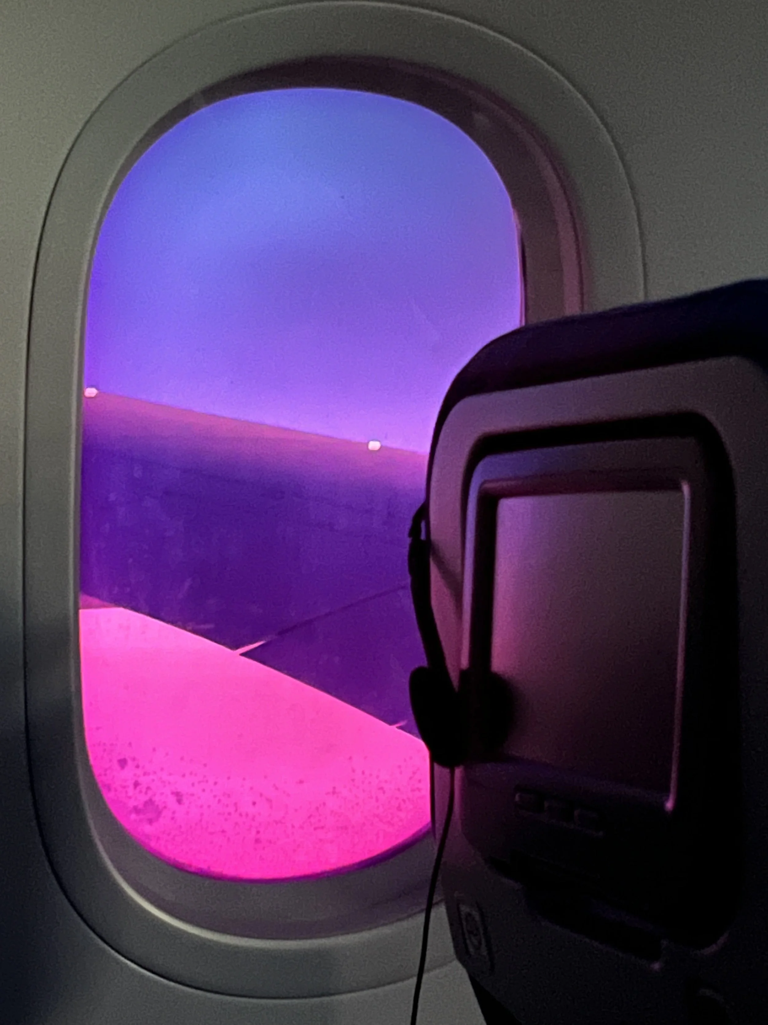 View through airplane window showing purple and pink sunset or sunrise sky with clouds.