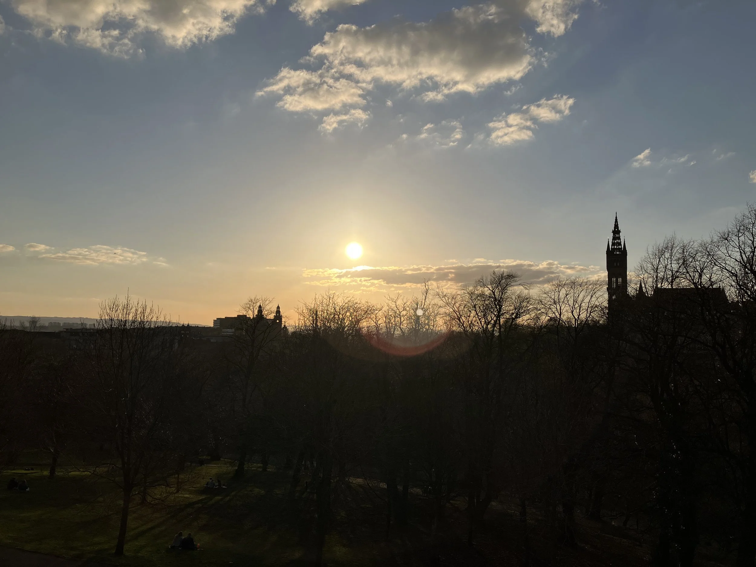 Sunset over a city with a church tower and trees in the foreground.