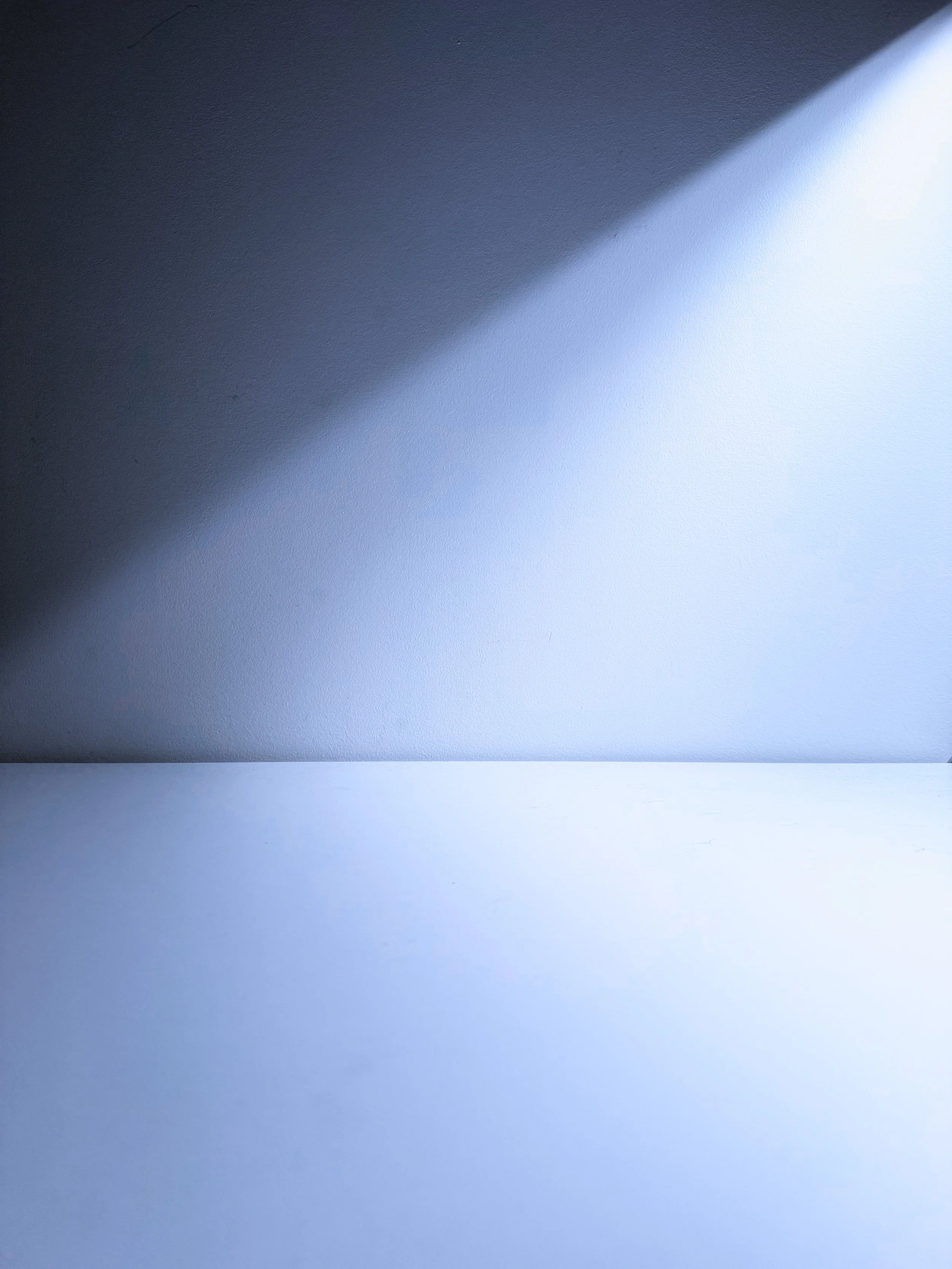 Close-up of a light gray wall with a diagonal shadow created by sunlight coming through a window or opening.