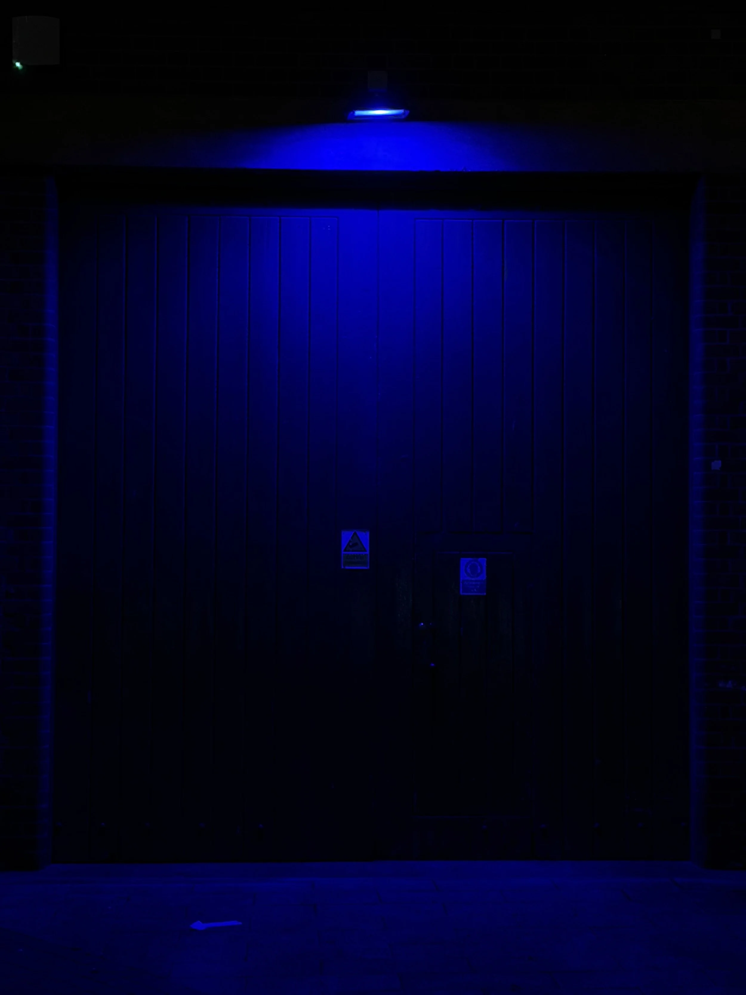 Garage door illuminated with blue light at night, with warning and information signs below.