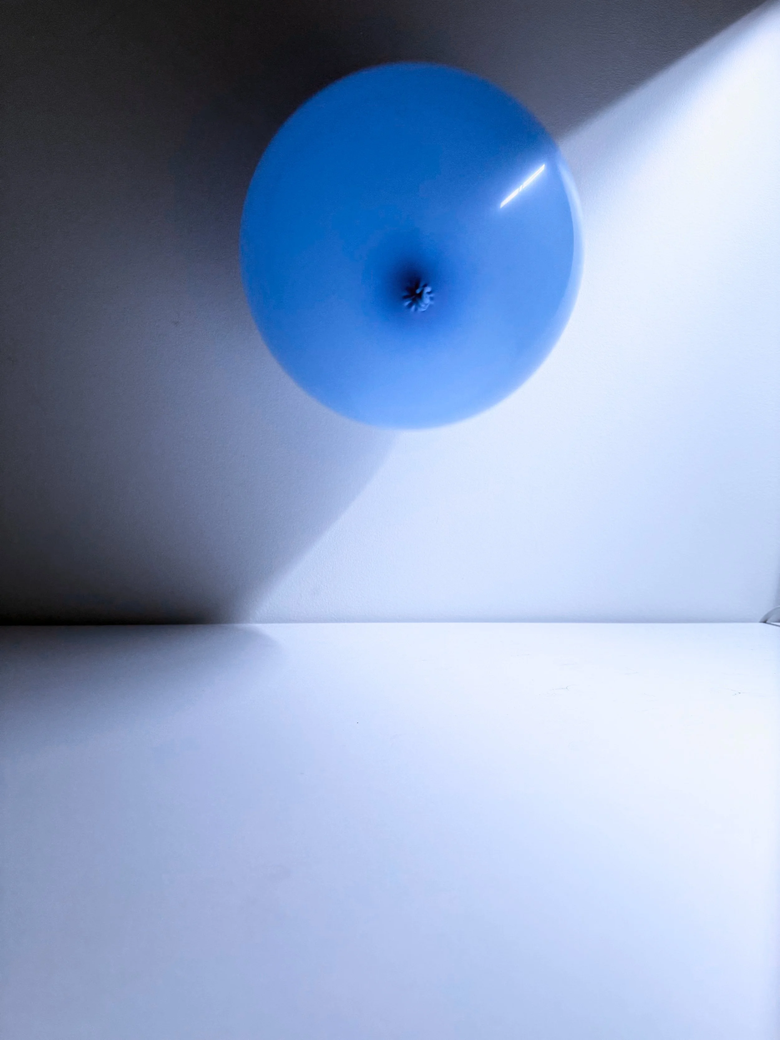 A blue teardrop-shaped object casting a shadow on a white surface, with a bright reflection on the upper right side.