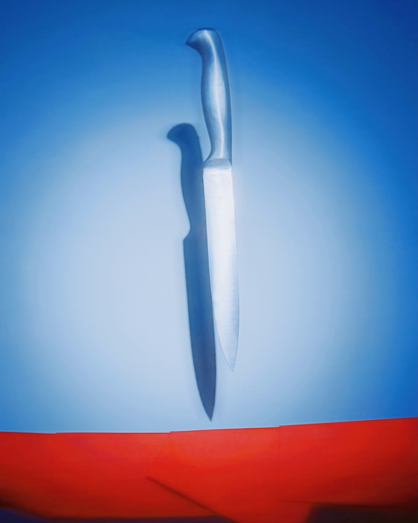 A sharp kitchen knife with a stainless steel blade and black handle crossed with another similar knife against a blue and red background.