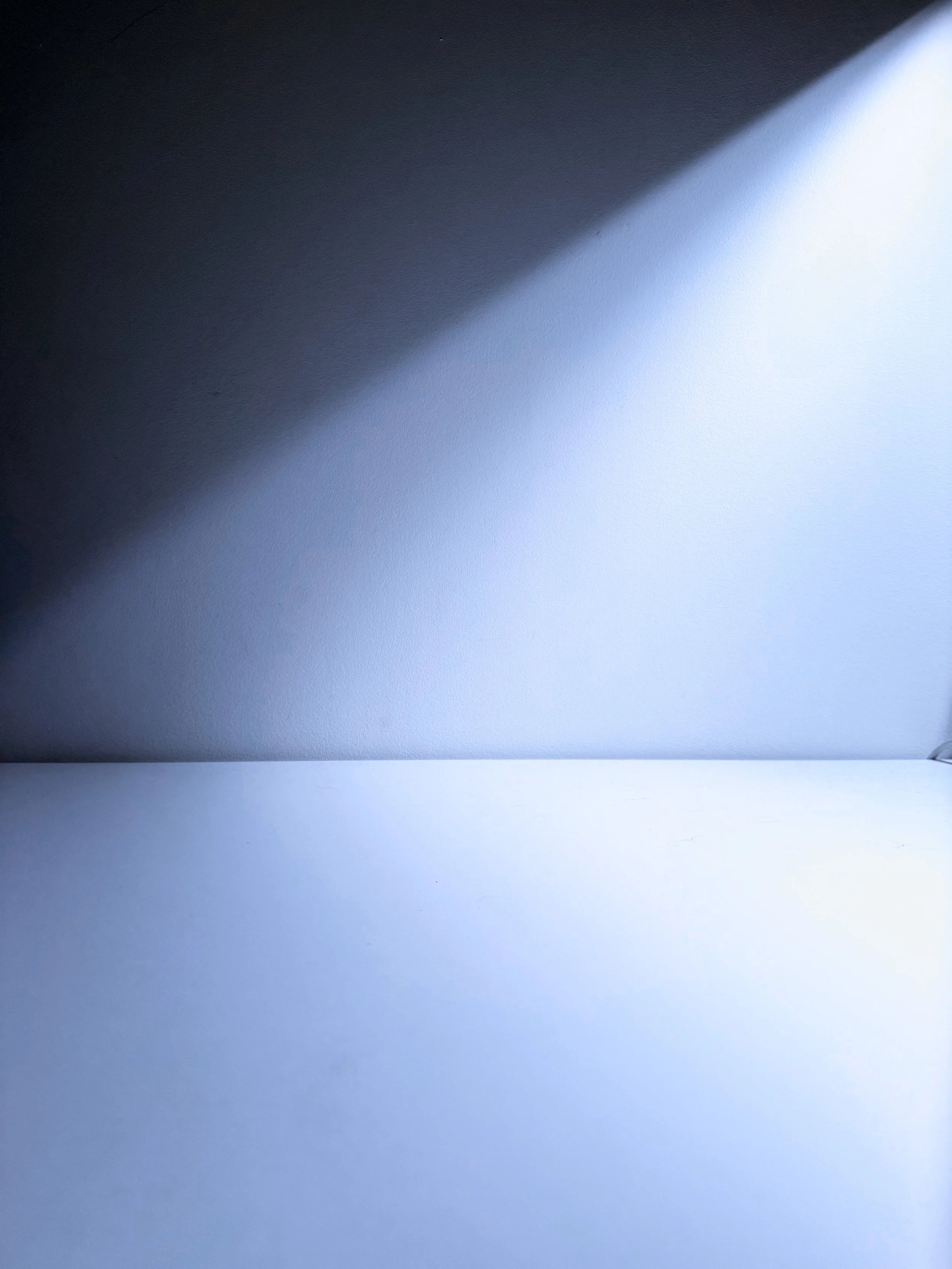 Close-up of a smooth, curved wall with a shadow cast at an angle, creating a gradient from dark to light.