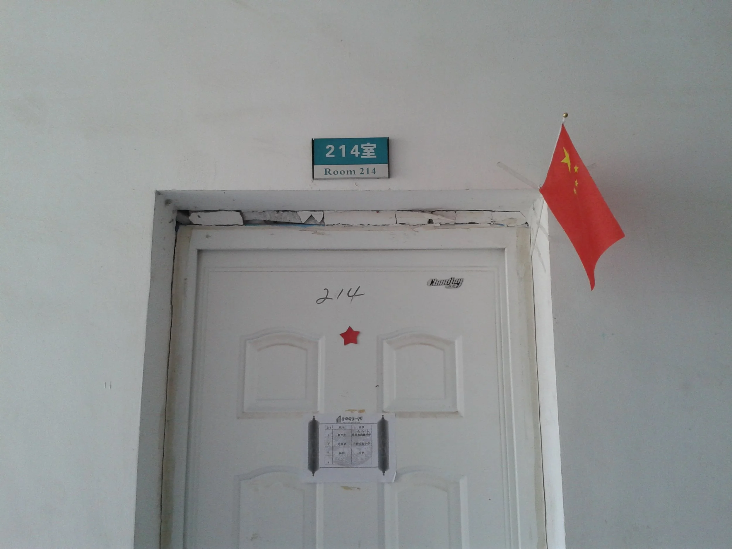 Indoor hallway with a white door, a blue and white sign indicating room 214, and a Chinese flag hanging on the wall.