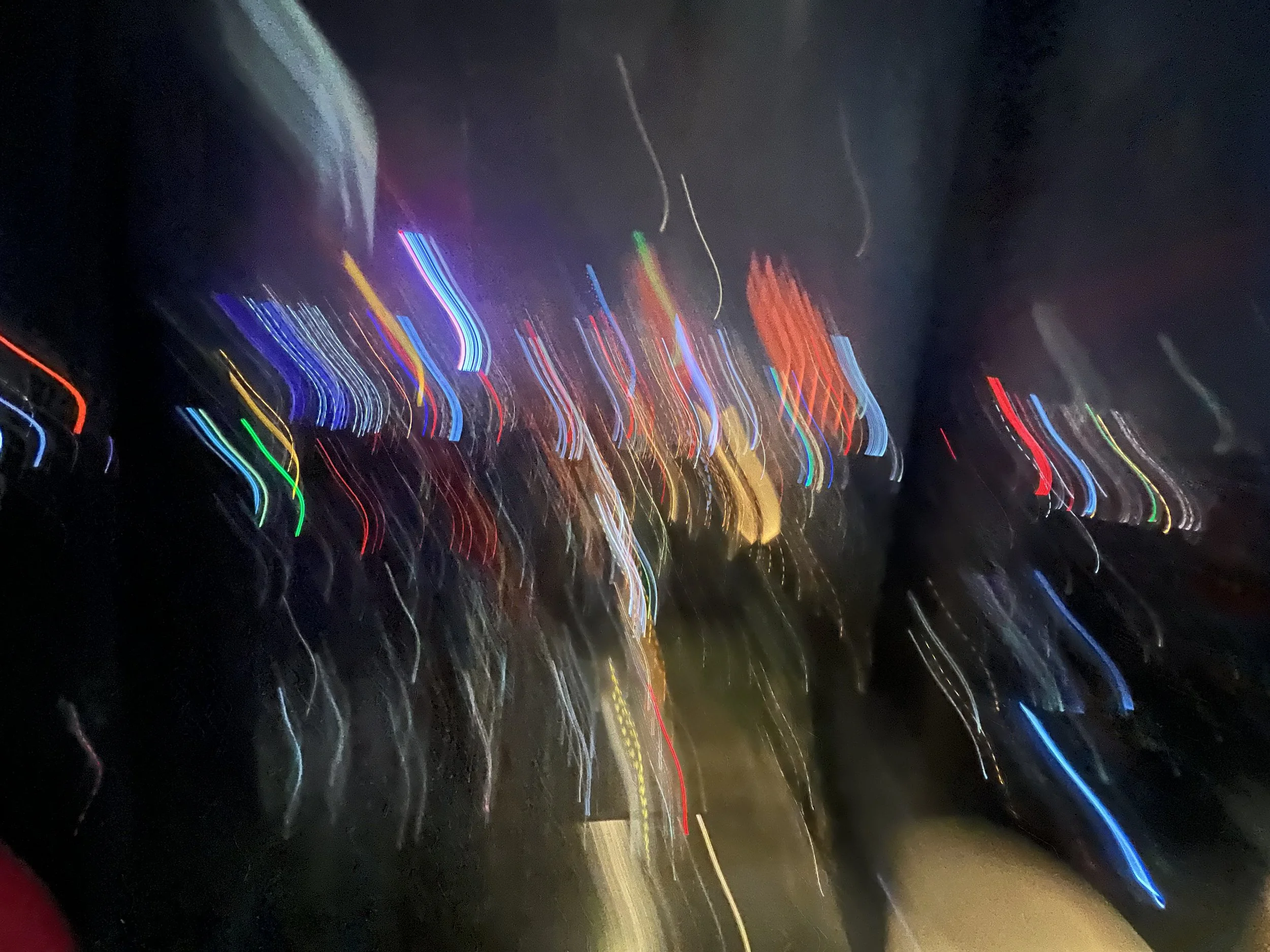 Blurry nighttime city street with streaks of colorful lights from moving vehicles.
