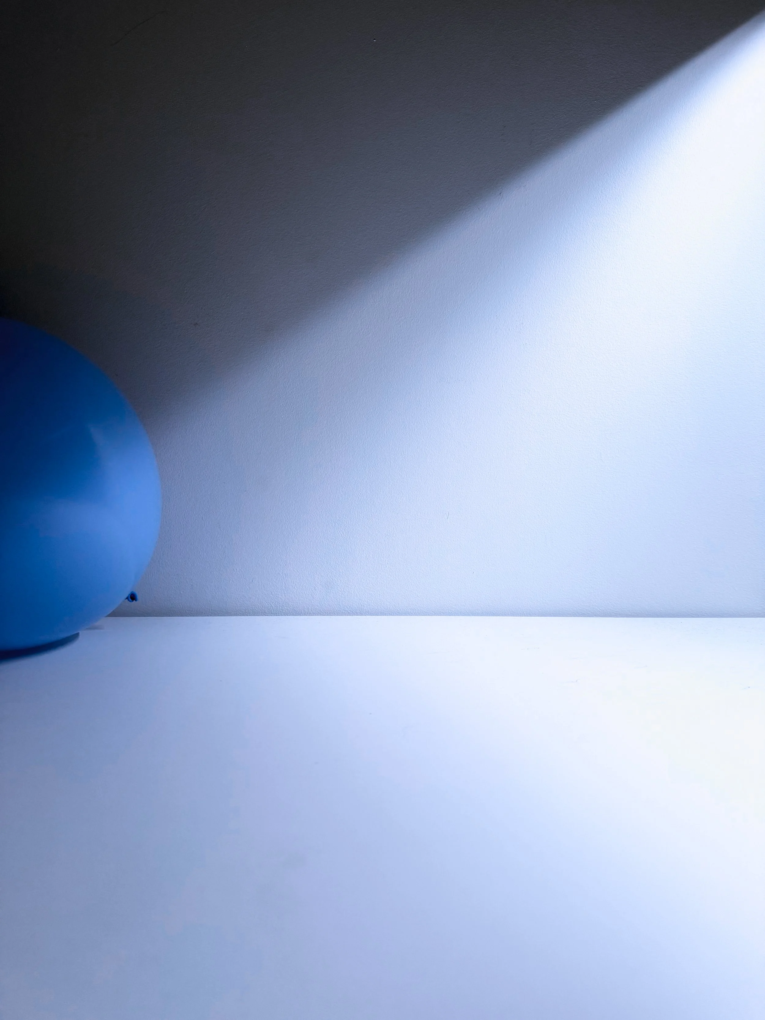 Blue balloon partially visible on the left side of the image, on a surface with a light and shadowed background.