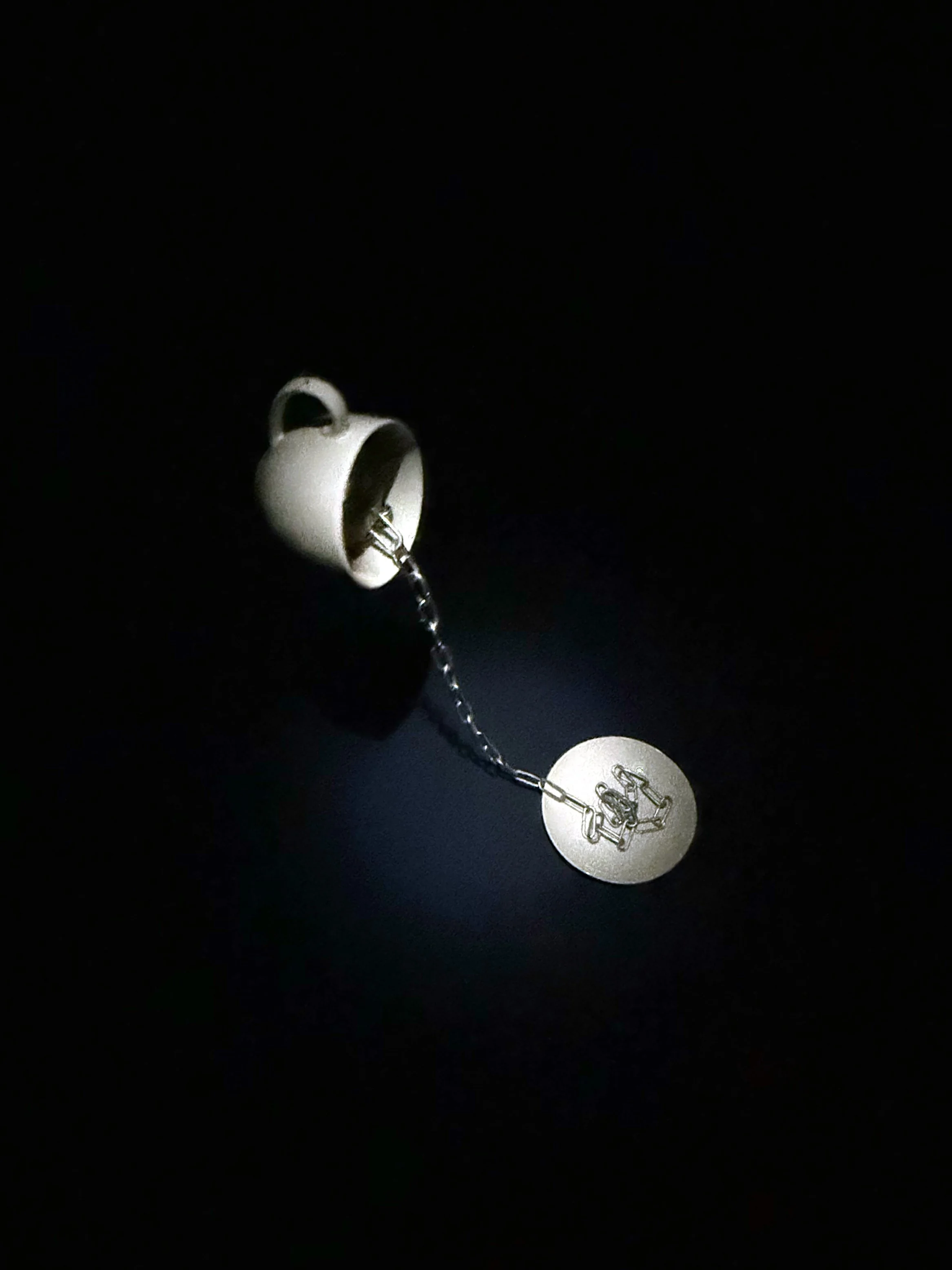 A white ceramic coffee cup is pouring coffee into a saucer with a design, against a black background.