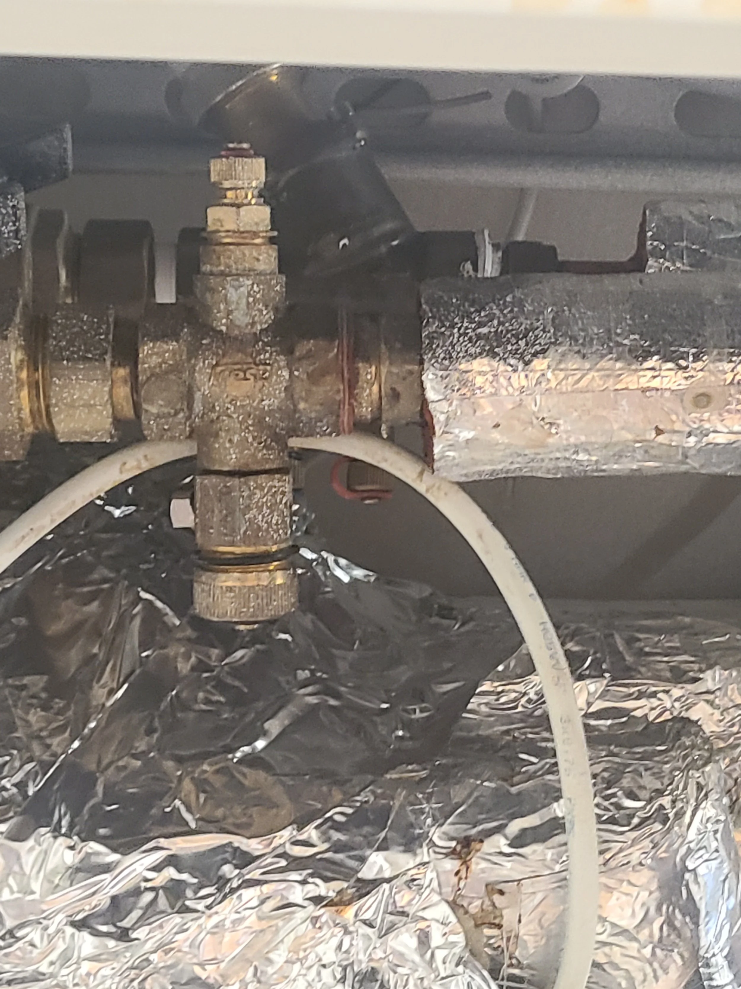 Close-up of a mechanical part with rusted metal, a white tube, and aluminum foil-like material underneath.