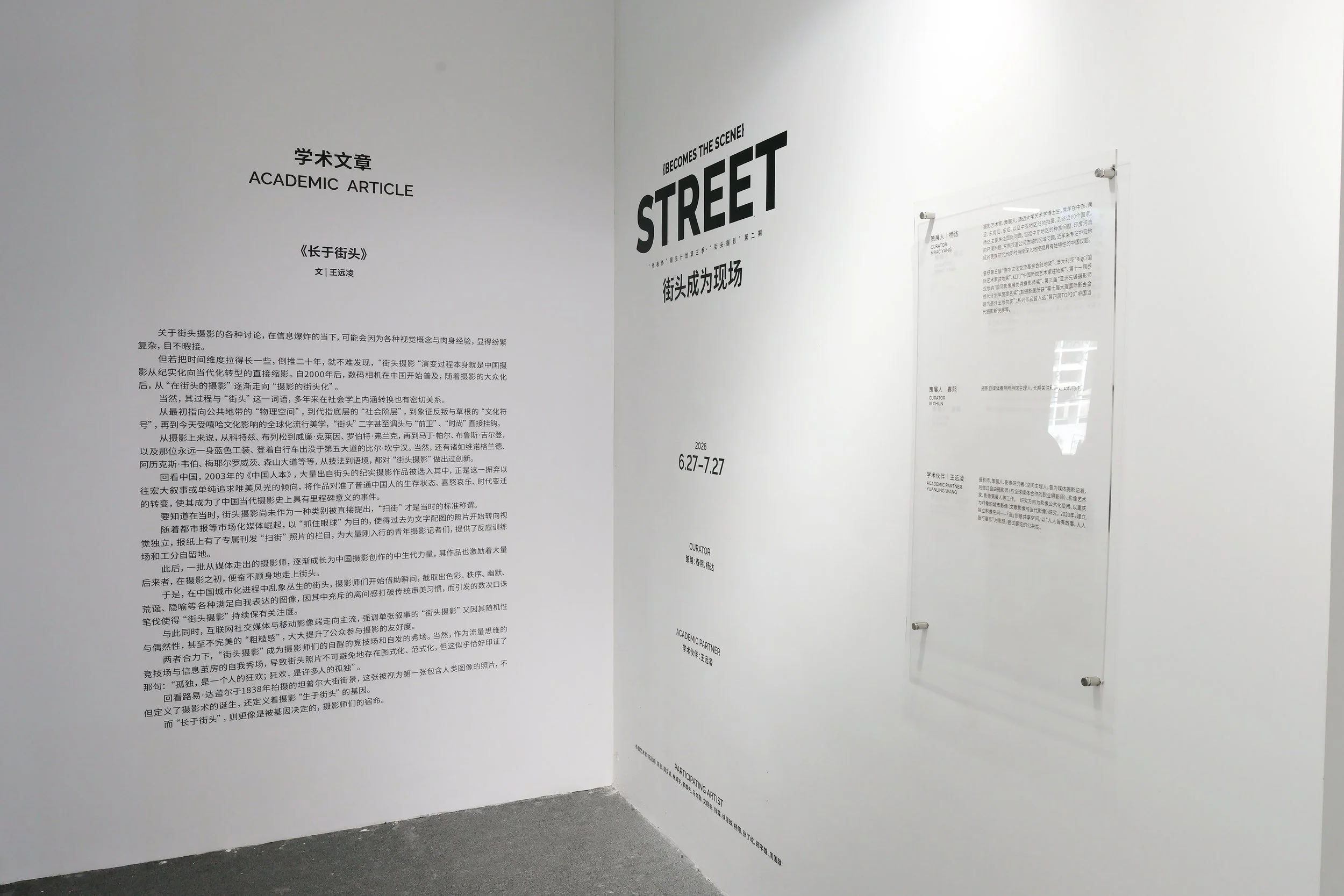 An exhibition display with texts on white walls, including titles in English and Chinese about academic articles and street photography, with installation hardware visible.