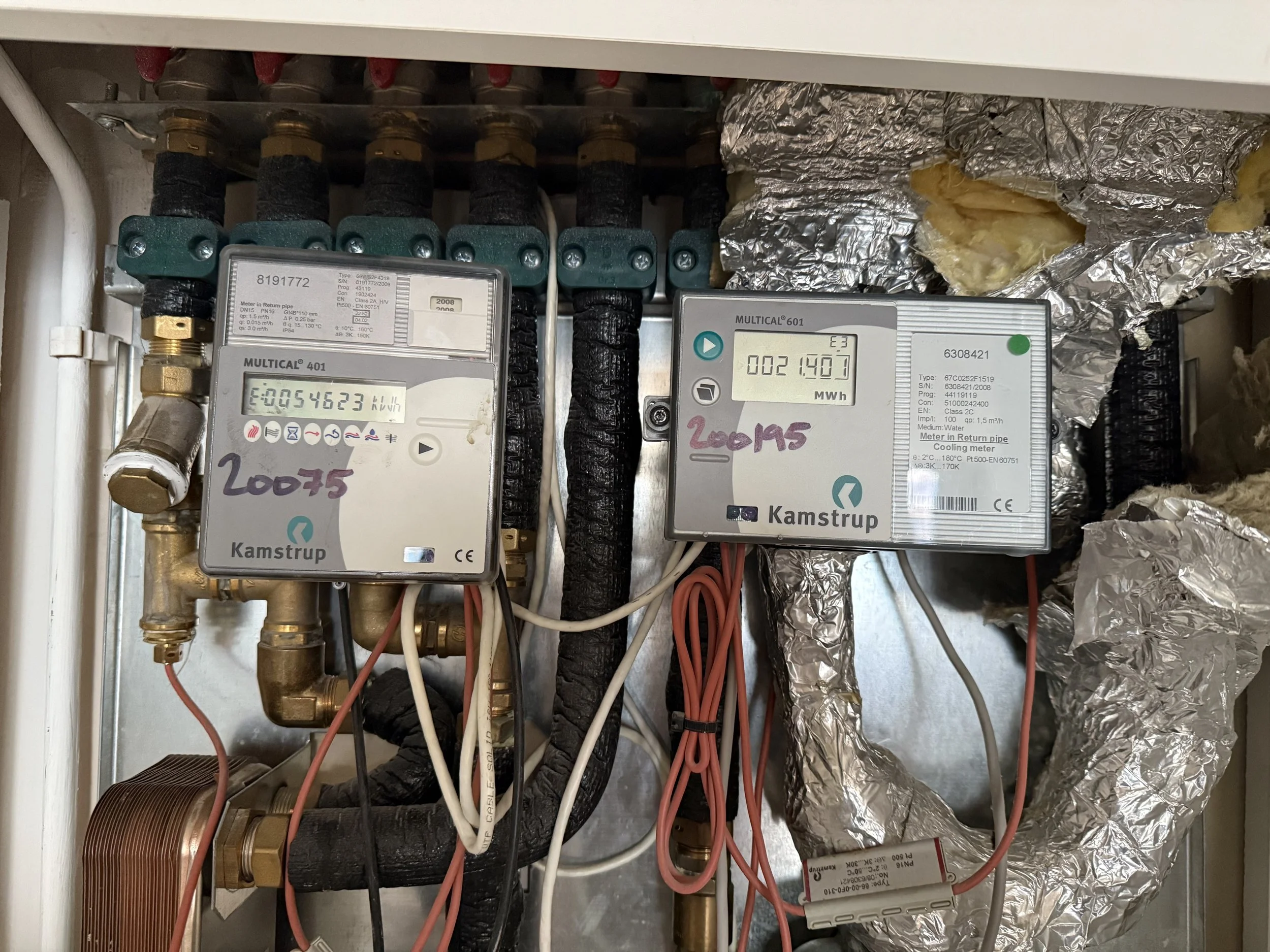 Electrical panel with meters, pipes, and wiring, partially covered with aluminum foil insulation.