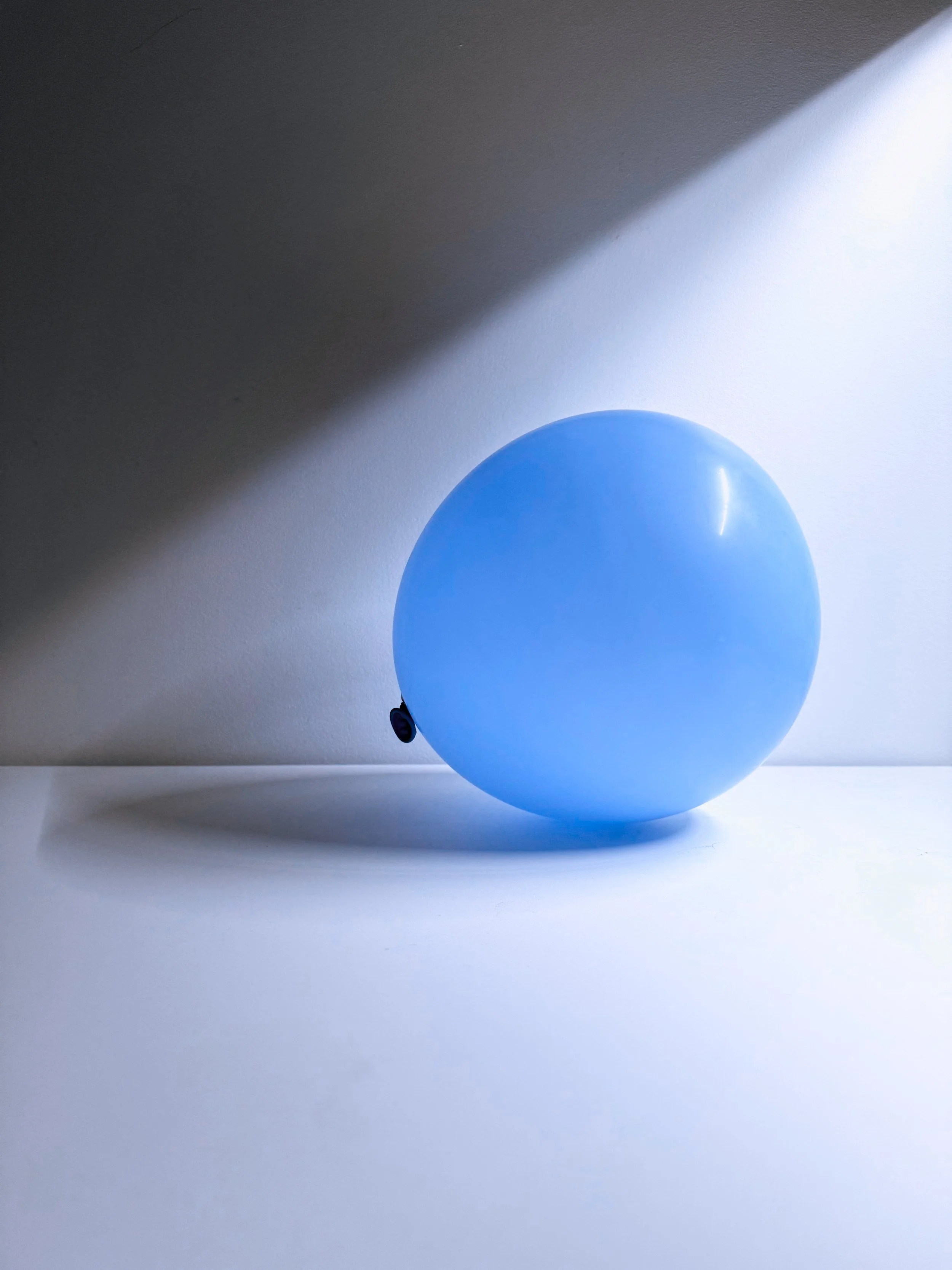 Blue balloon resting on a white surface with a light source creating shadow and glare.