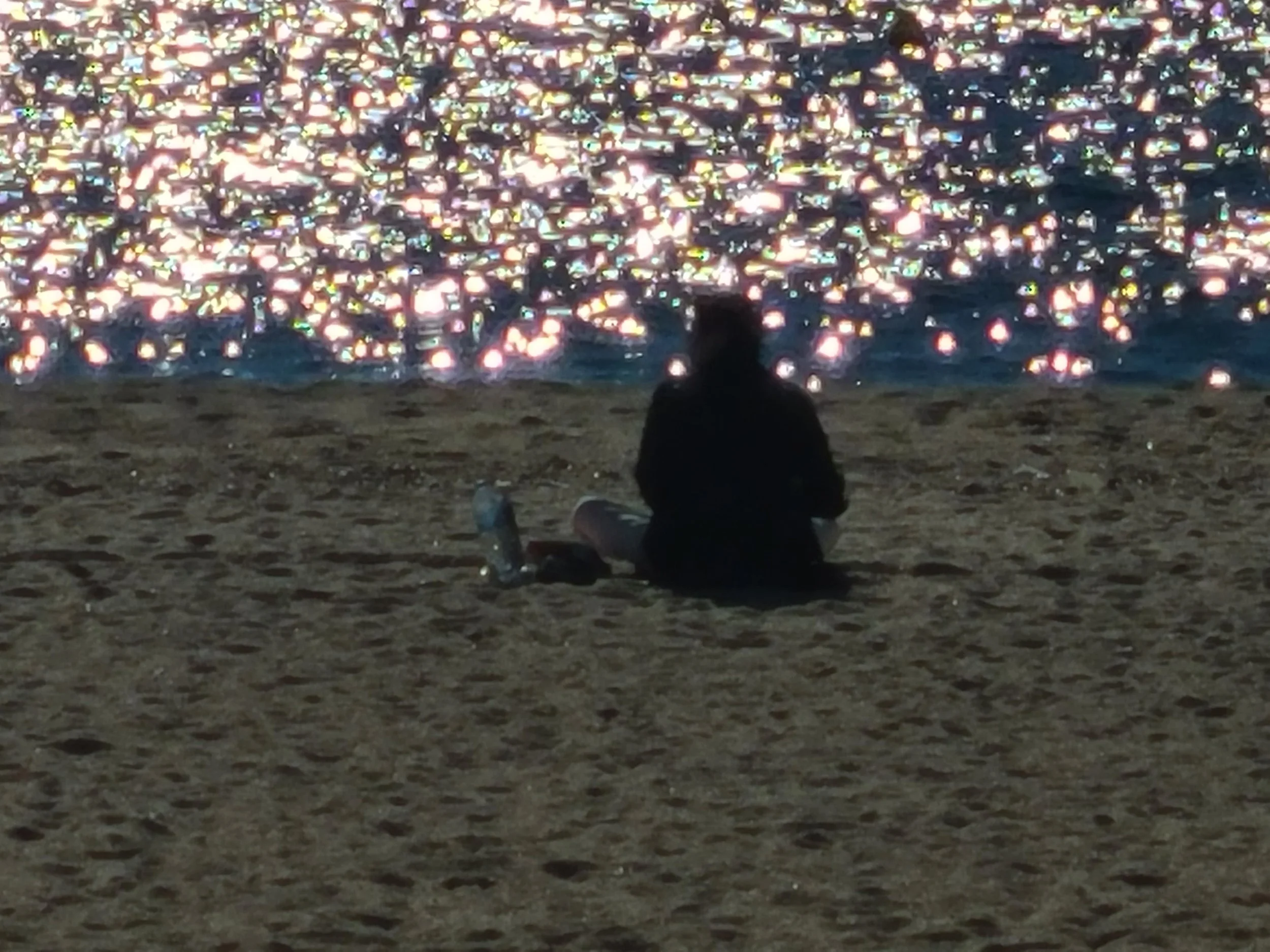A person sitting on the sandy beach at night, watching a large display of hundreds of floating lanterns in the sky.