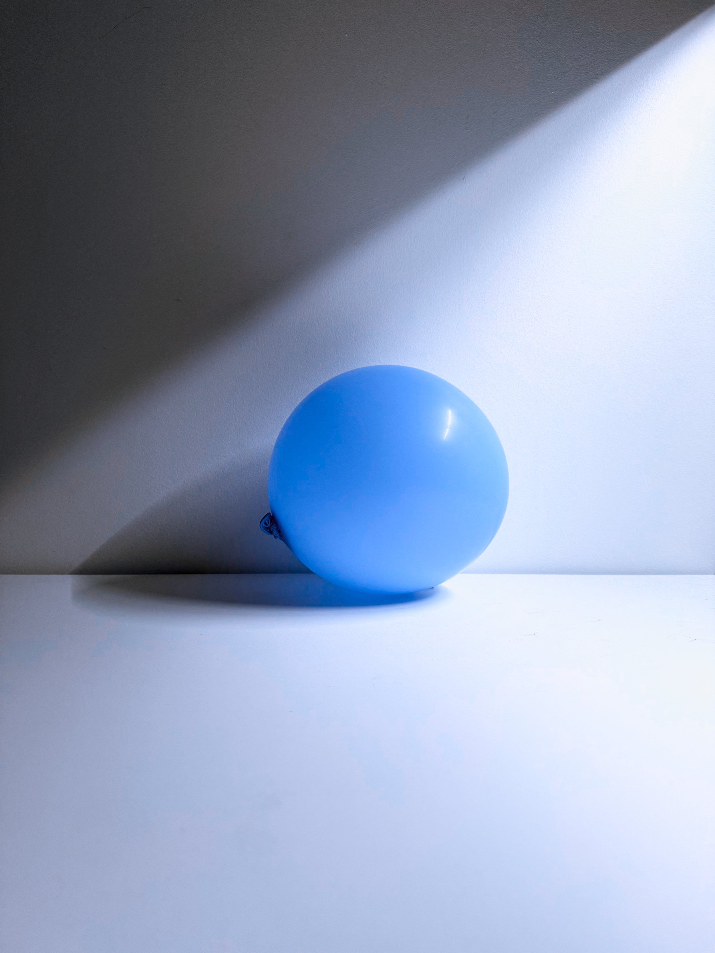 A single blue balloon on a white surface with a shadow cast on the background wall.