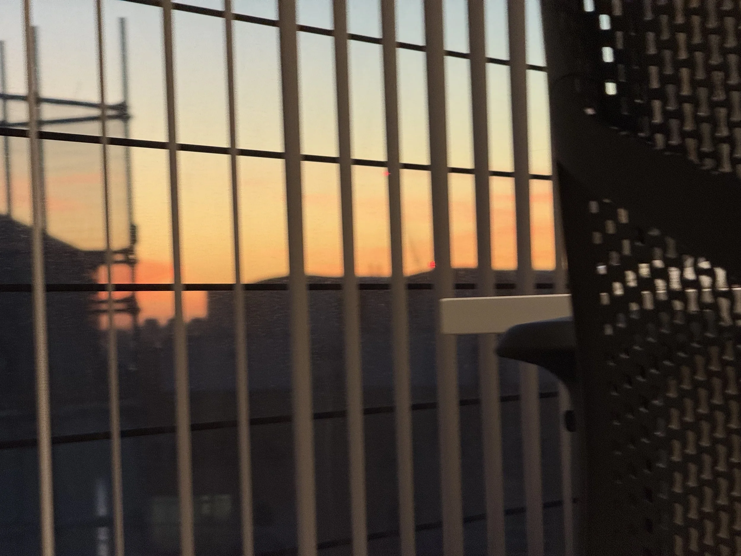 Close-up of a black metal balcony railing during sunset with a sunset sky in the background.