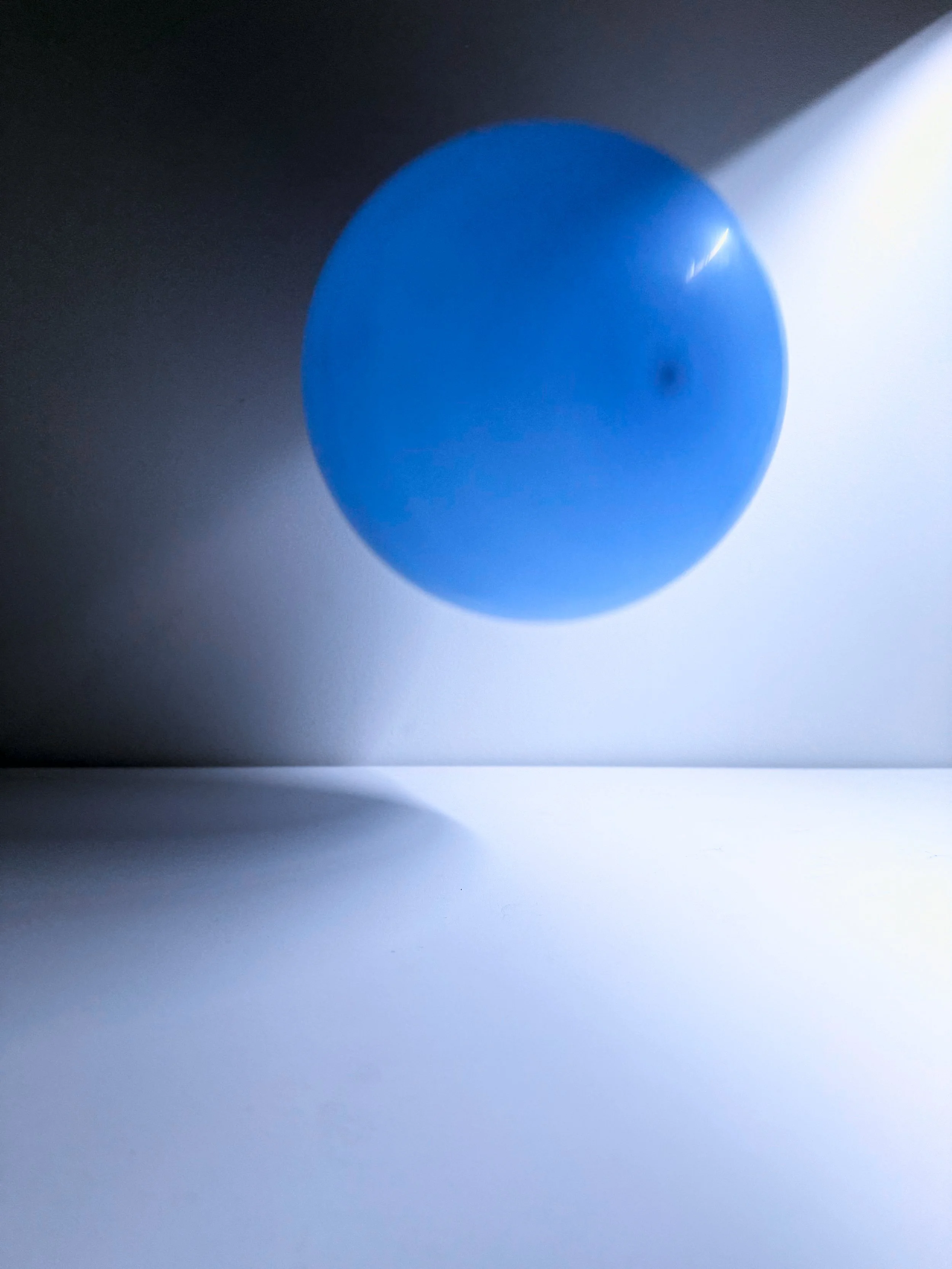 A blue spherical object cast a shadow on a white surface, with a light source shining from the upper right corner.
