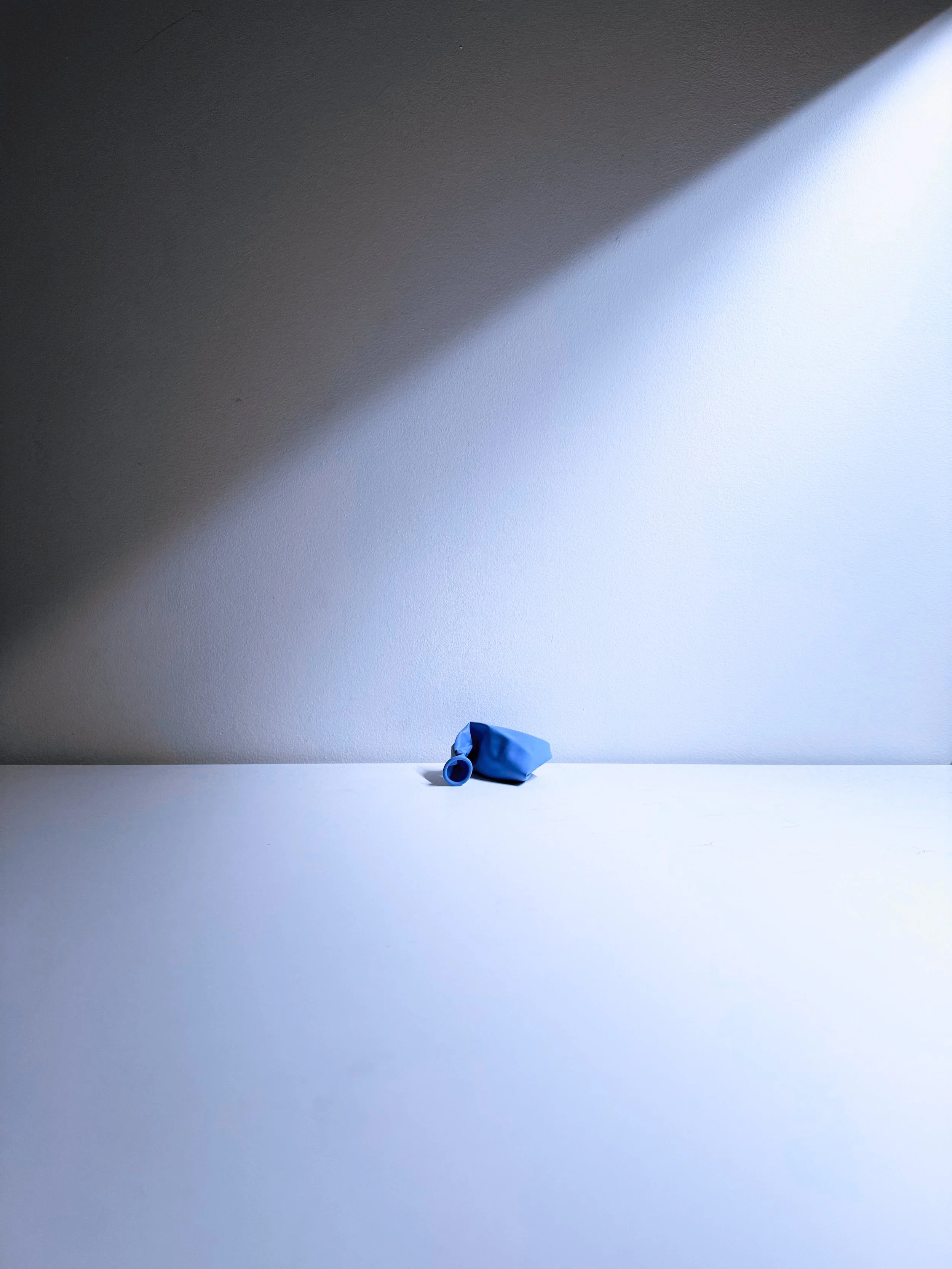 A small blue object sitting on a white surface, against a plain wall with a diagonal shadow dividing the wall into darker and lighter sections.