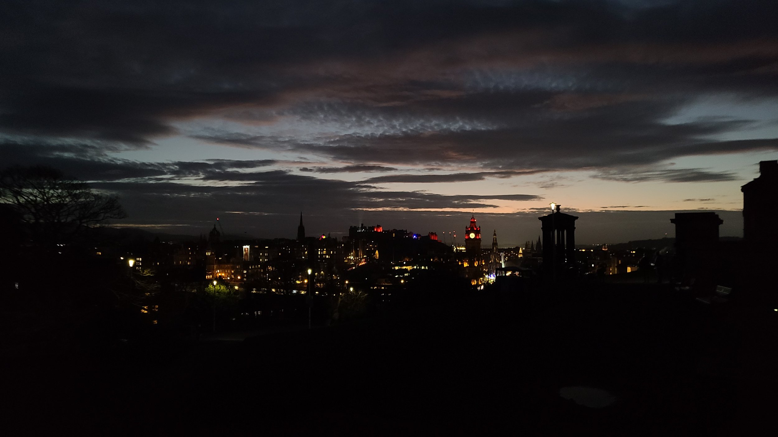 City skyline at dusk with illuminated buildings, clock tower, and cloudy sky