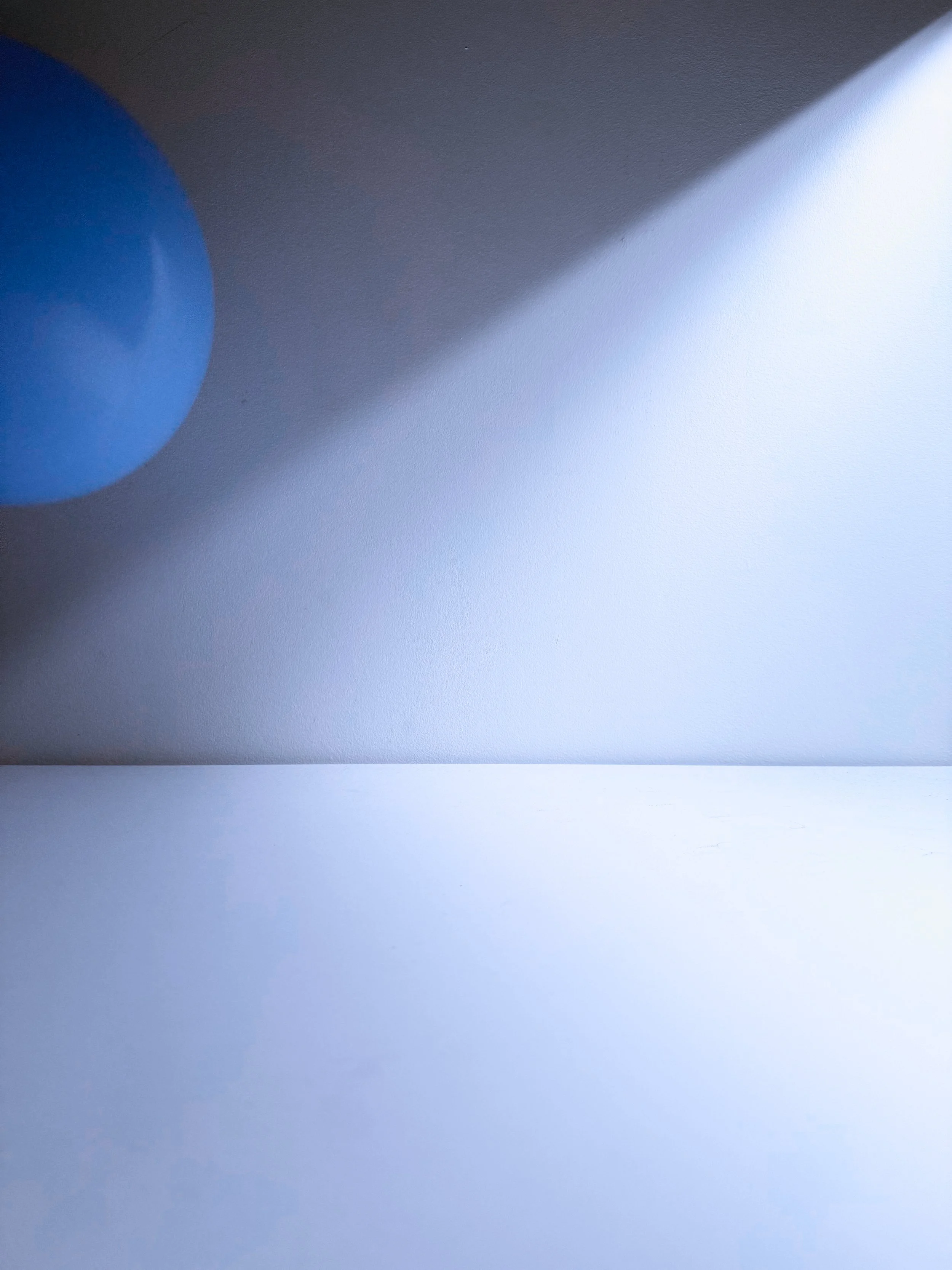 A close-up of a blue balloon on a white surface, casting a shadow and with a textured wall background.